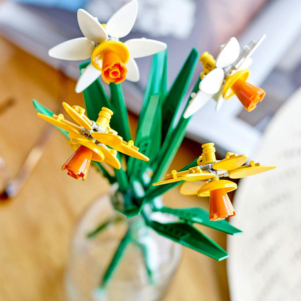 Lego-Osterglocken in einer Vase. Drei Blüten mit weißen Blütenblättern, orangefarbenen Zentren und grünen Stielen.