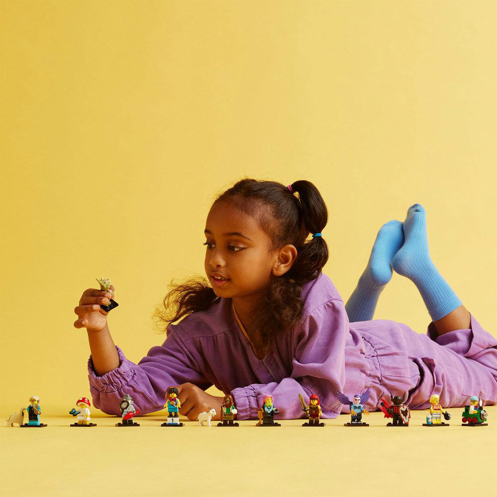 Ein junges Mädchen liegt auf gelbem Untergrund mit Lego-Figuren. Einige Figuren sind scharf.