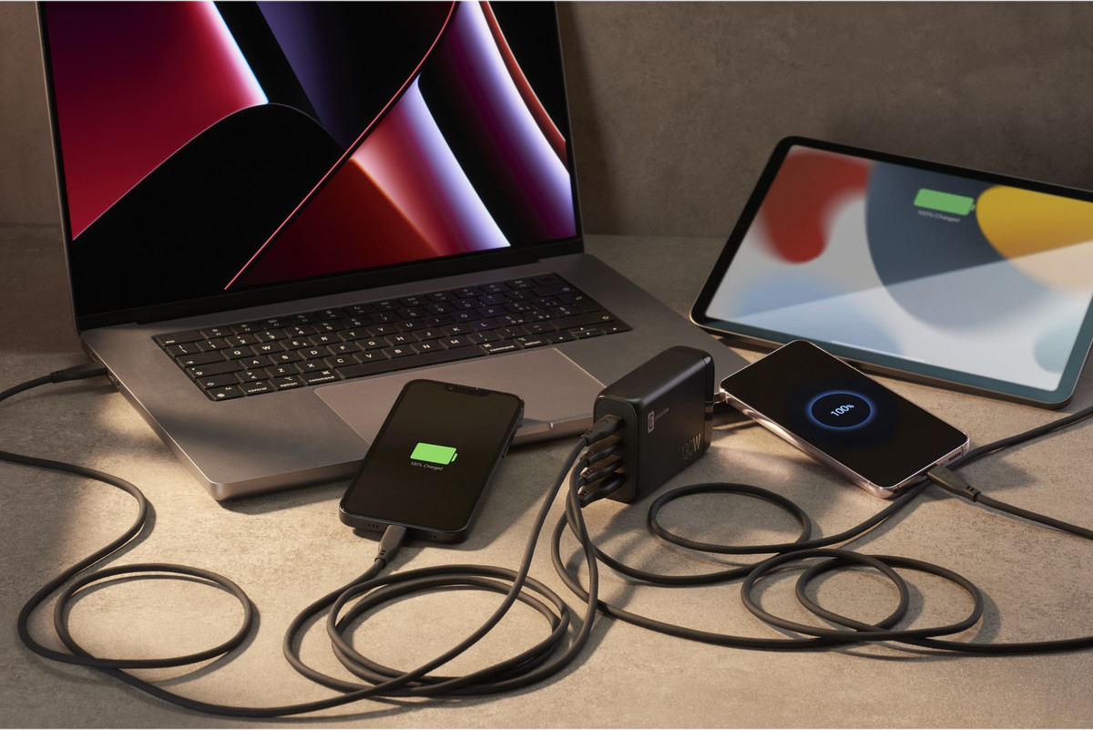 Ein Laptop, ein Tablet und zwei Telefone, die geladen werden. Laptop und Tablet stehen auf einem Schreibtisch.