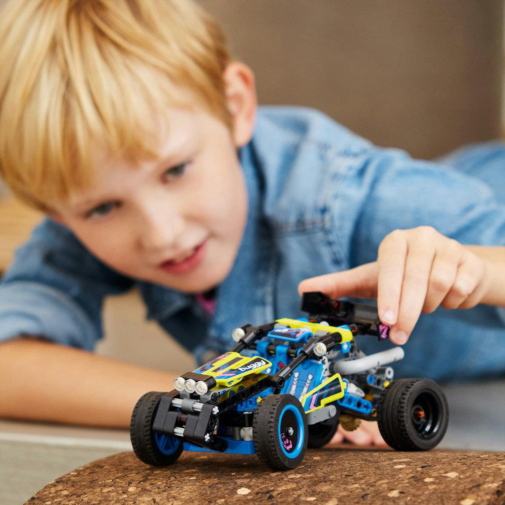 Junge spielt mit einem blau-gelben Spielzeugauto, mit einem lächelnden Gesichtsausdruck.