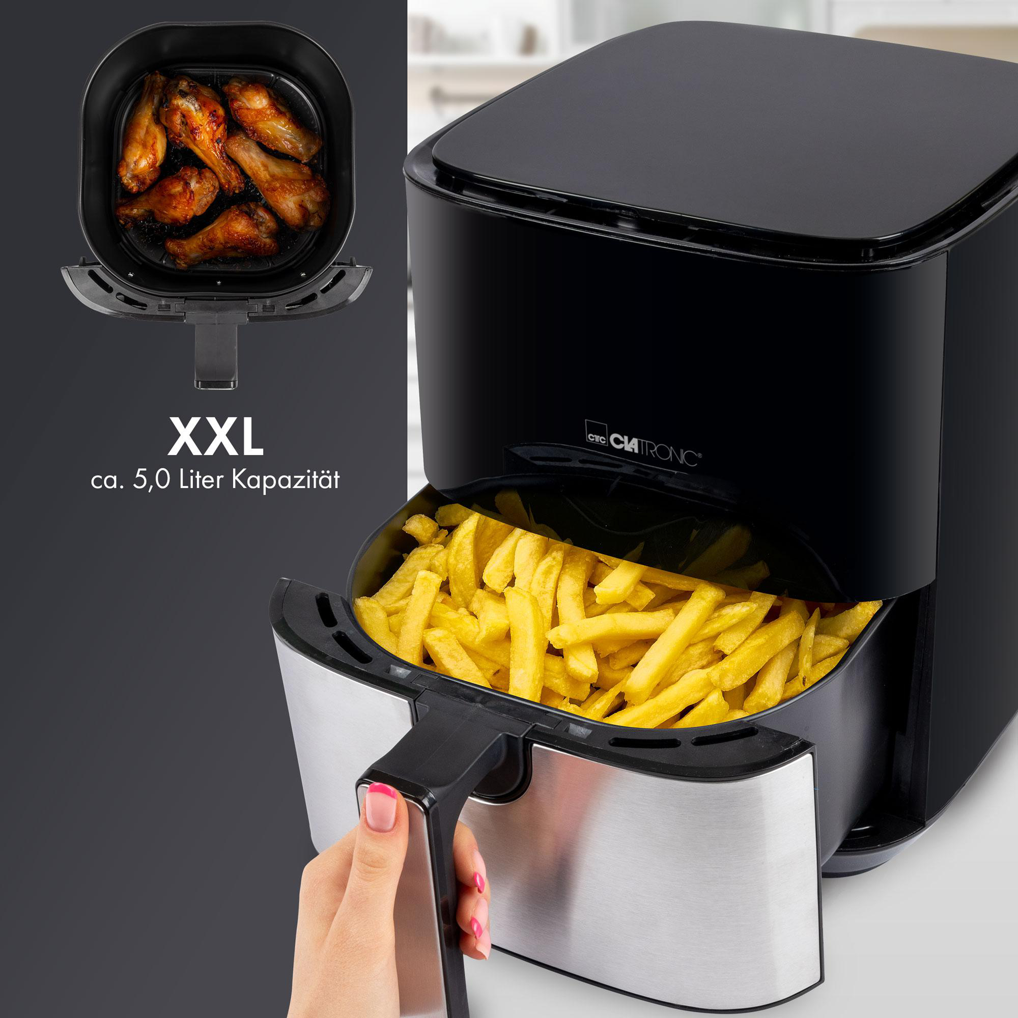 Schwarze Heißluftfritteuse mit Pommes im Korb, Flügeln im Behälter, Hand am Griff.