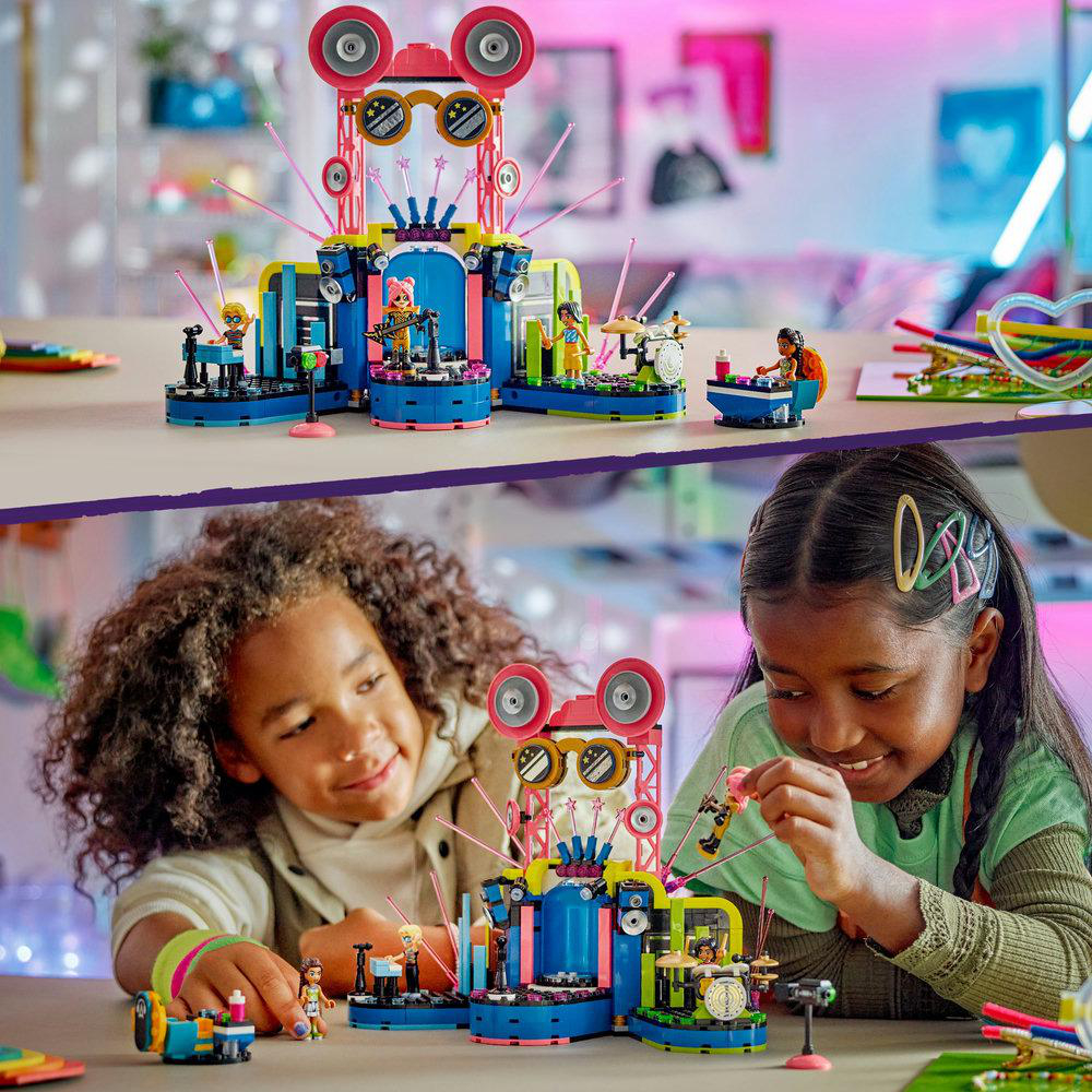 Lego-Set mit Figuren, Bühne, Lautsprechern. Zwei Mädchen spielen mit dem Set auf einem Tisch.