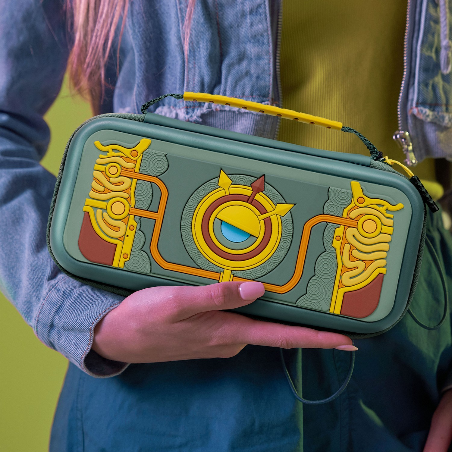 A green and black case for a Nintendo Switch, held by a hand, yellow strap.