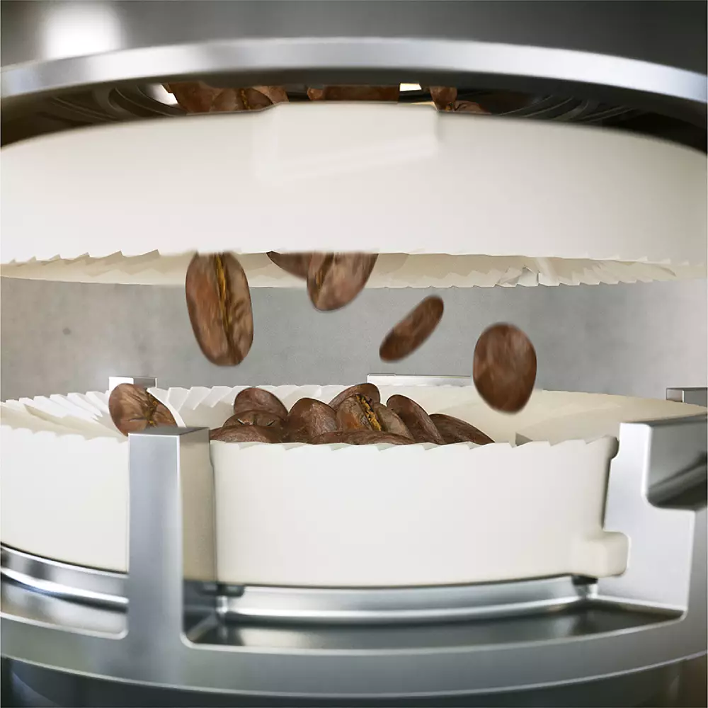 Primer plano de granos de café cayendo en un molinillo de café. El molinillo es blanco con partes plateadas.