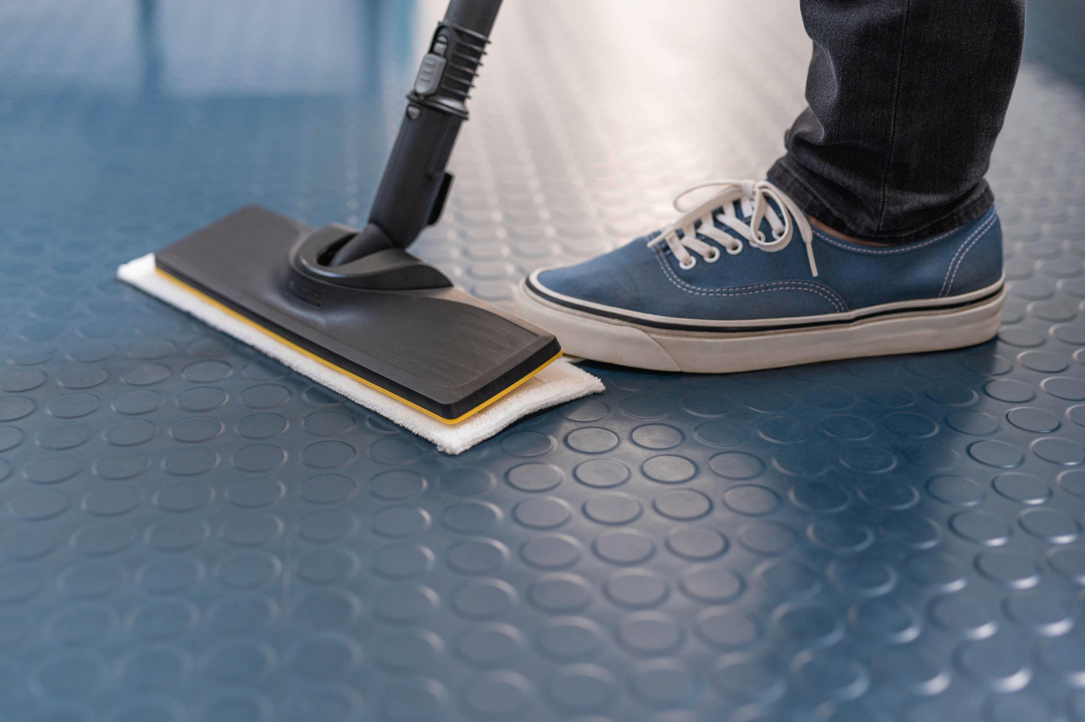 Person reinigt blauen Boden mit einem Wischmopp. Blaue Schuhe sichtbar.
