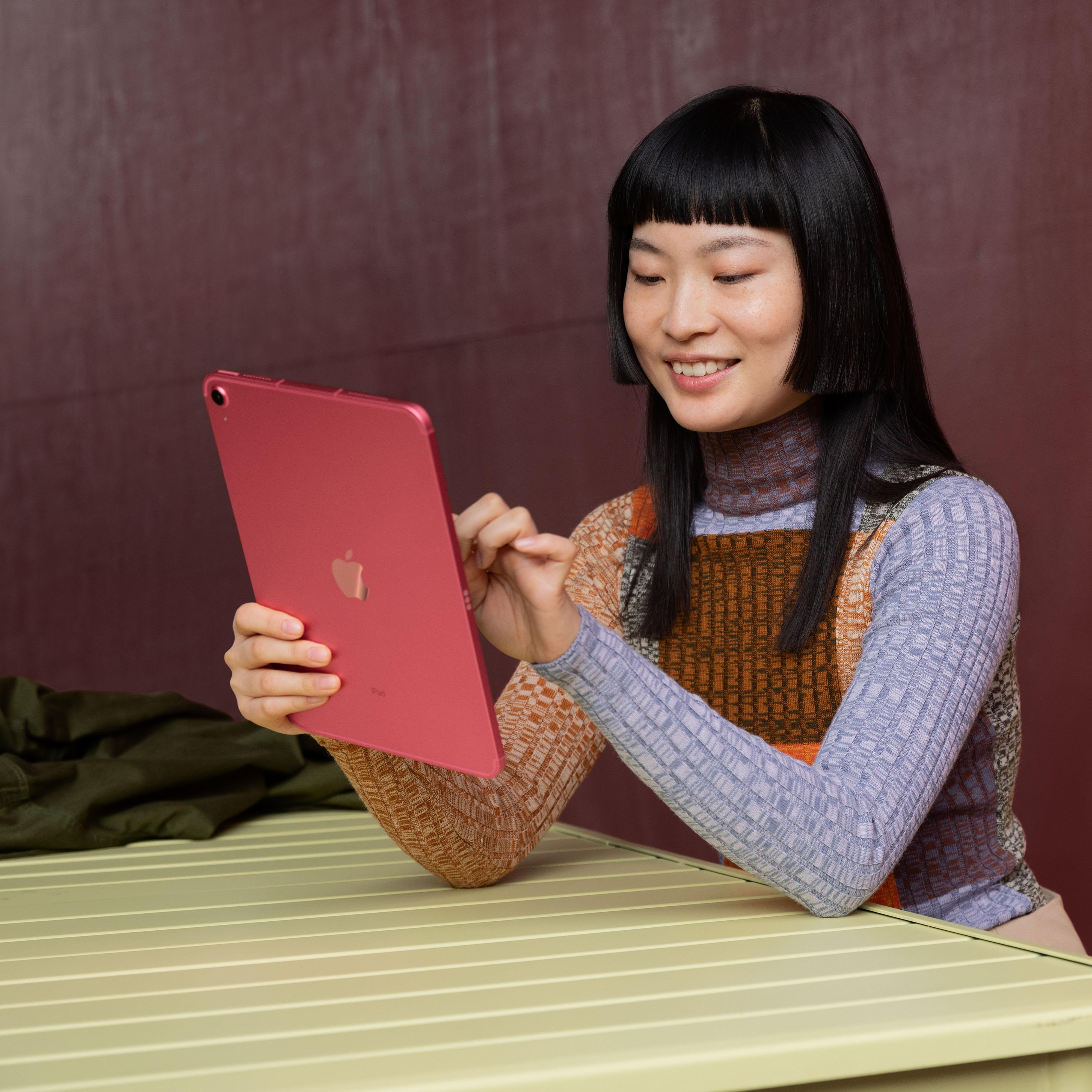 Eine Frau mit schwarzen Haaren benutzt ein rotes Tablet, während sie an einem gelben Tisch sitzt.