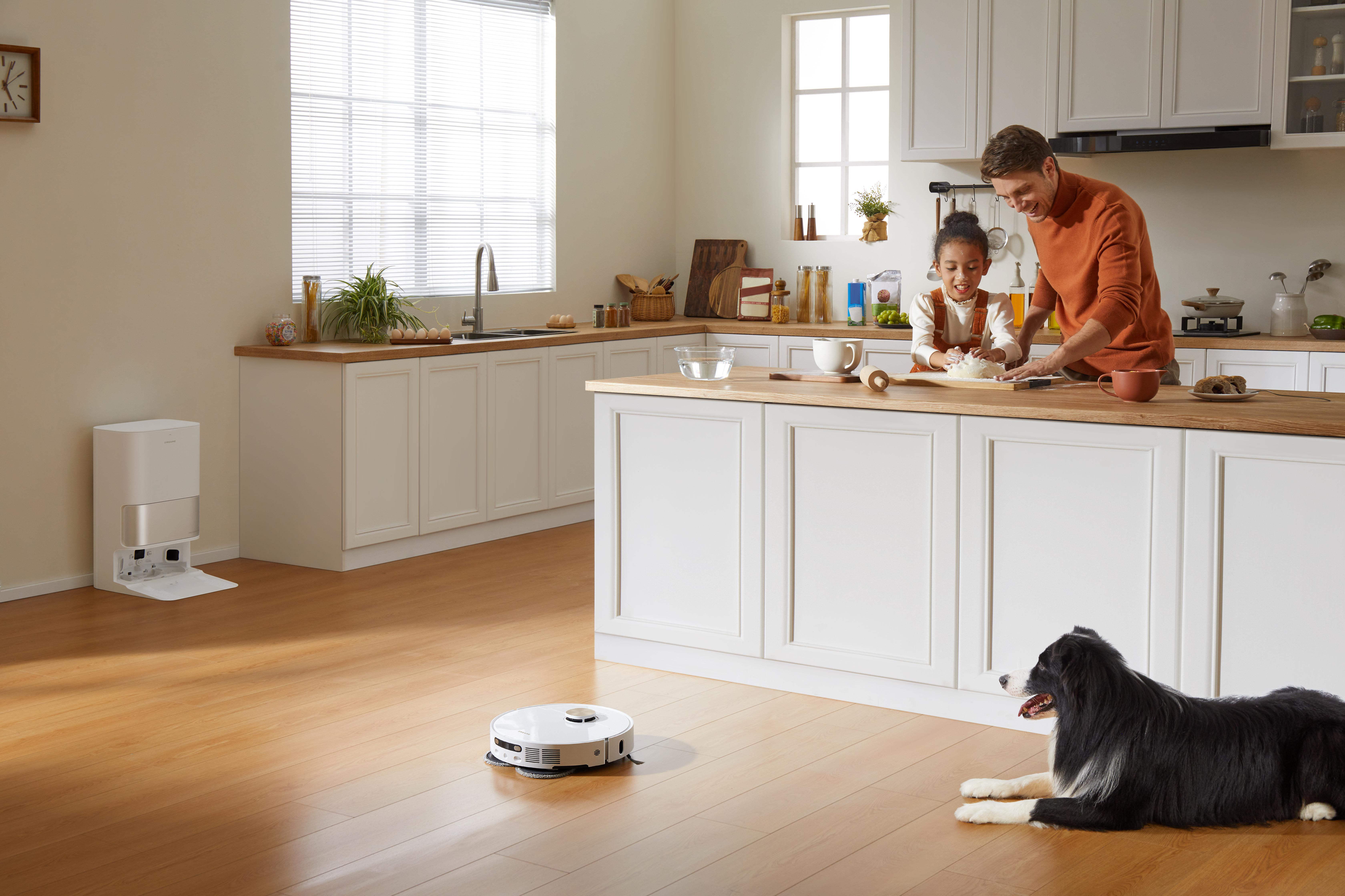 Eine Küche mit einer Frau und einem Kind, die Essen zubereiten, einem Roboterstaubsauger und einem Hund.