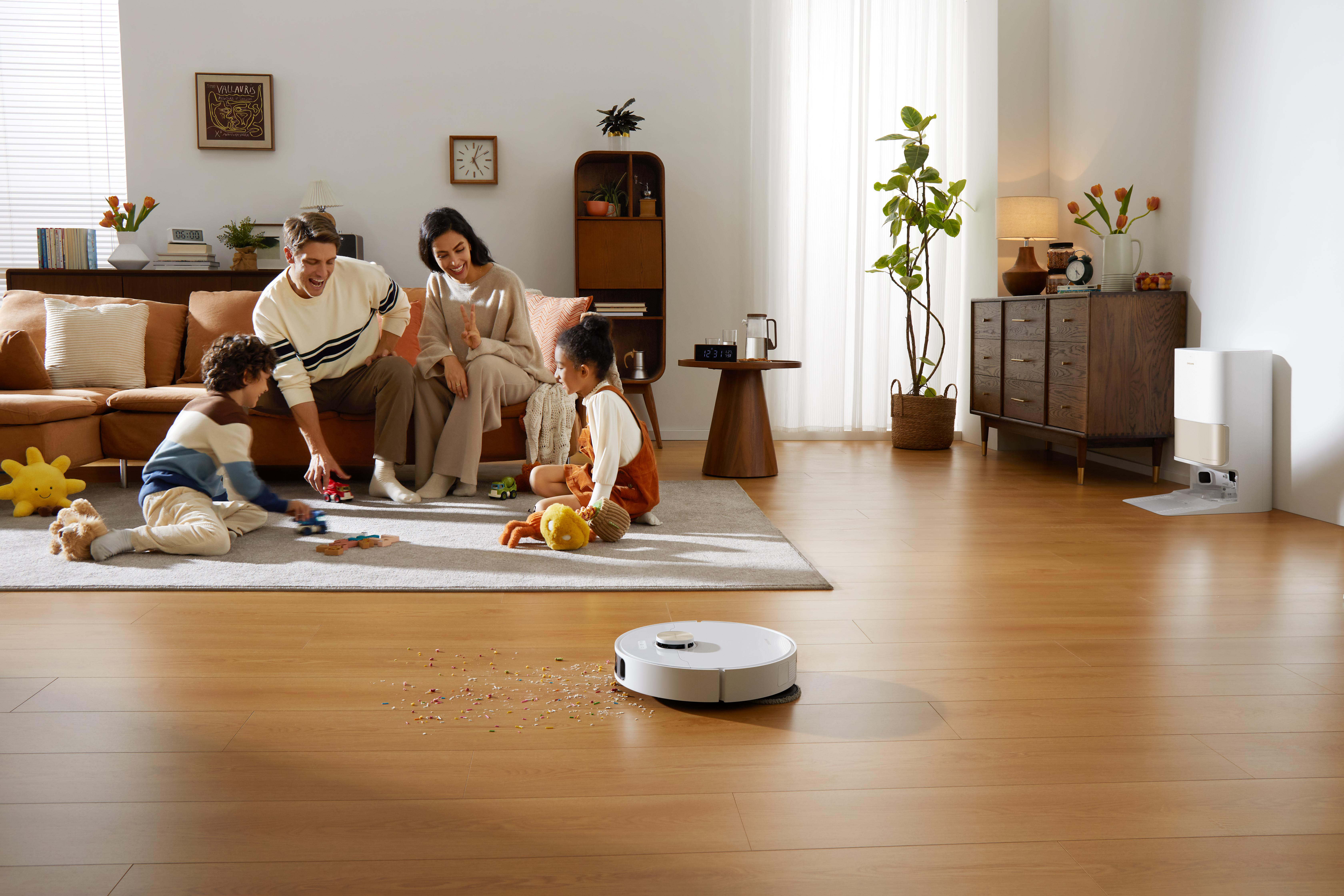 Familie im Wohnzimmer, Staubsaugen mit einem Roboter-Staubsauger auf dem Boden.