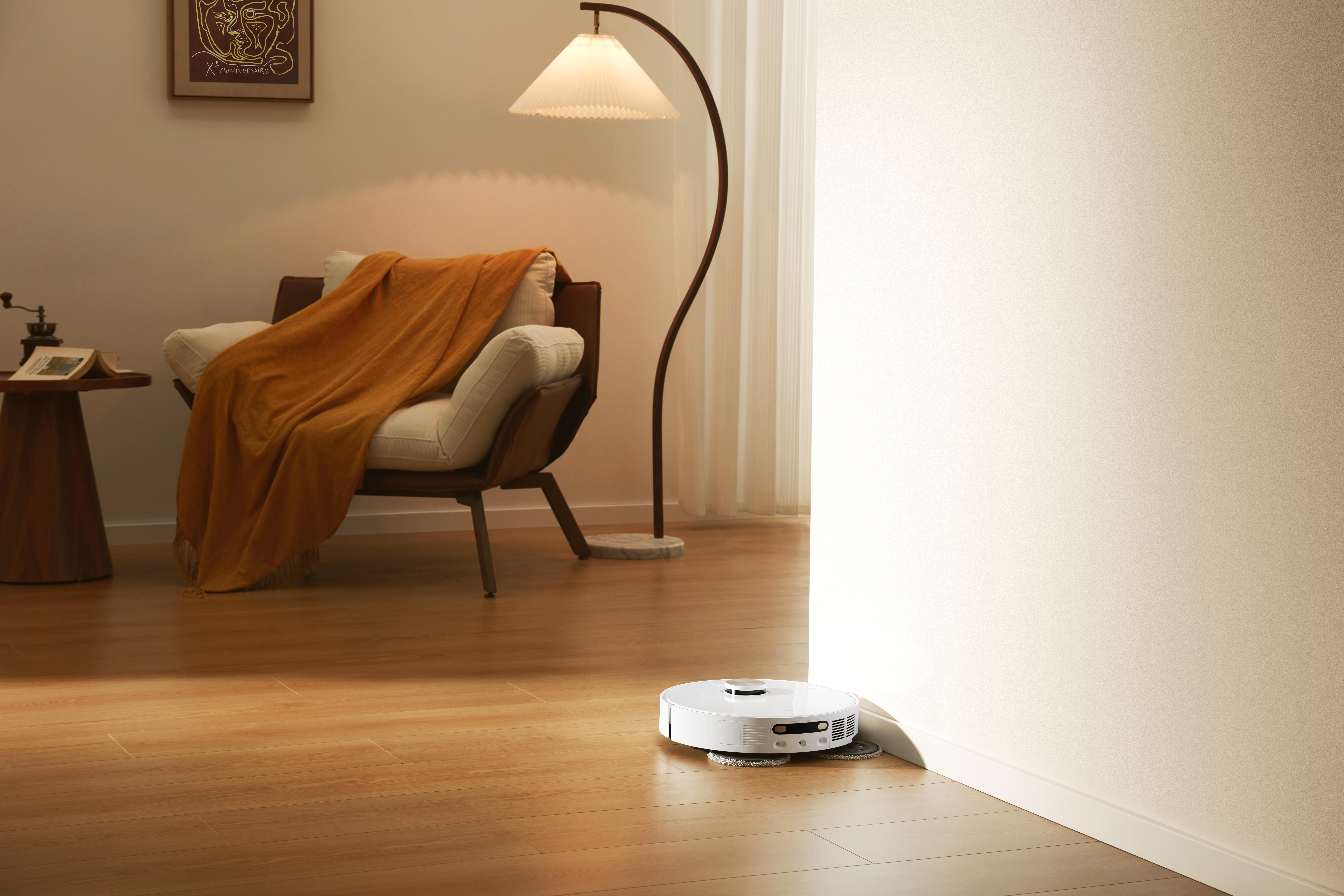 Raum mit weißem Roboter-Staubsauger. Es hat einen Holzboden, einen Stuhl und eine Lampe.