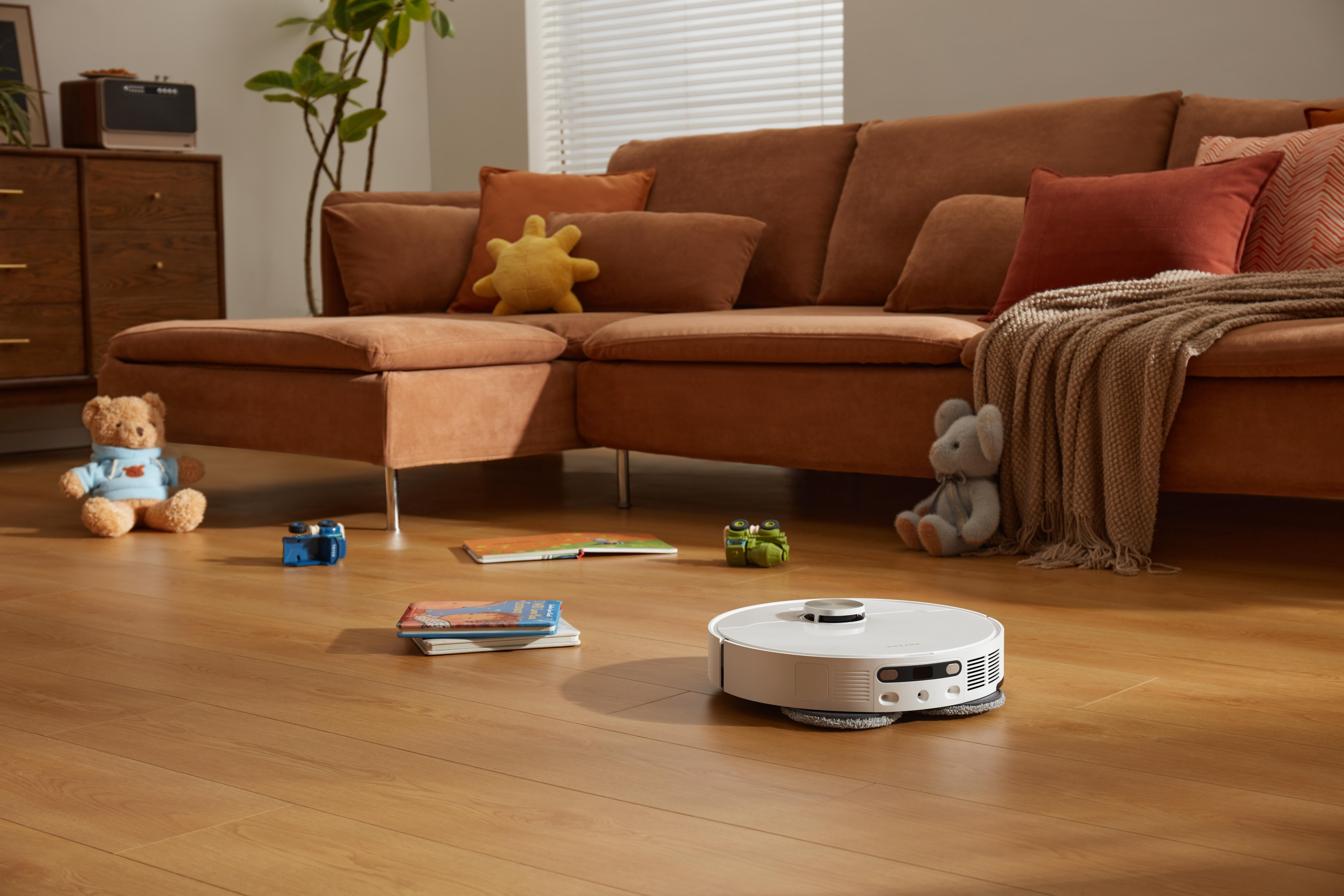 Roboter-Staubsauger auf Holzboden mit Spielzeug und Sofa.
