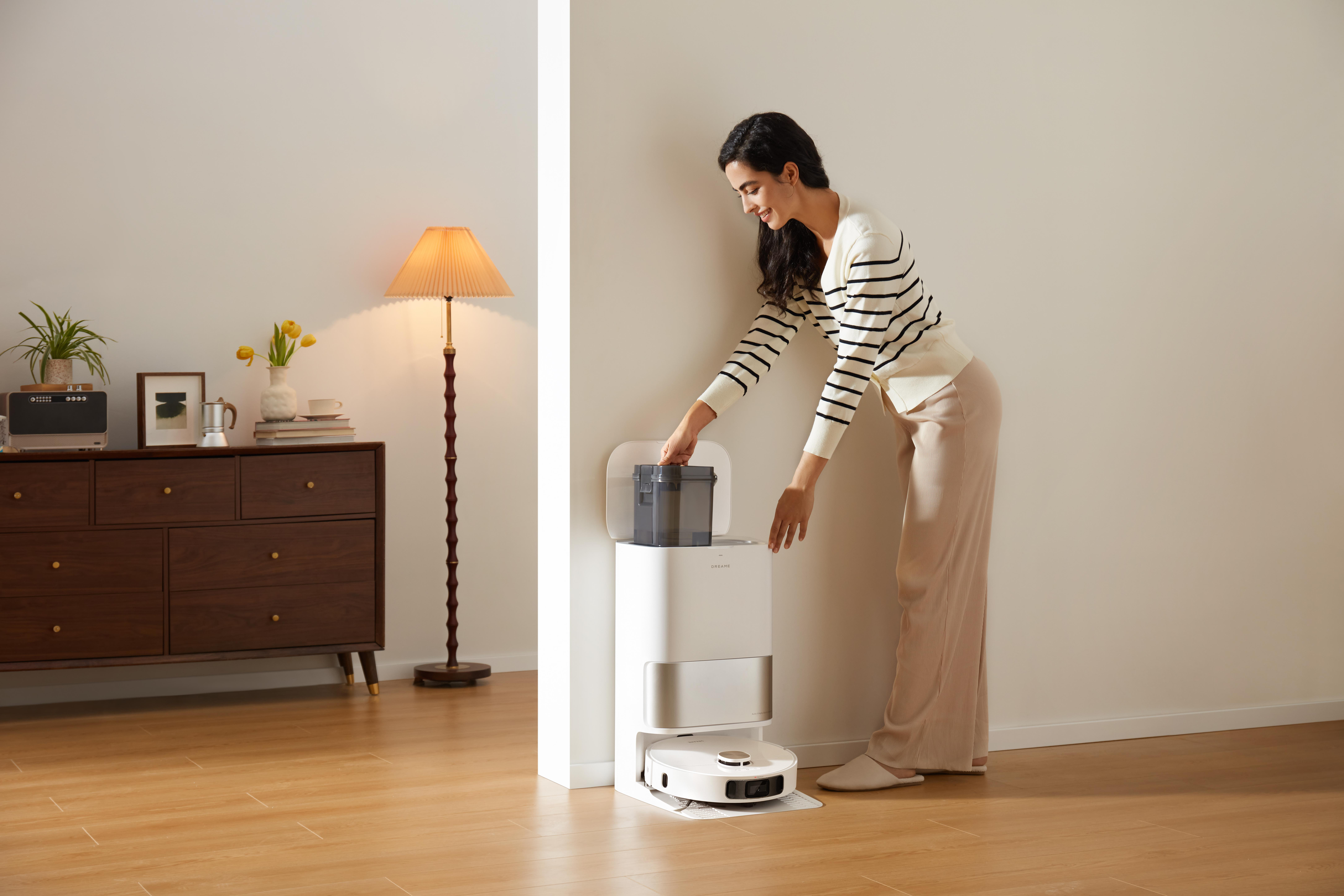 Frau setzt einen Behälter in einen Roboter-Staubsauger. Die Szene ist ein moderner, gut beleuchteter Raum.