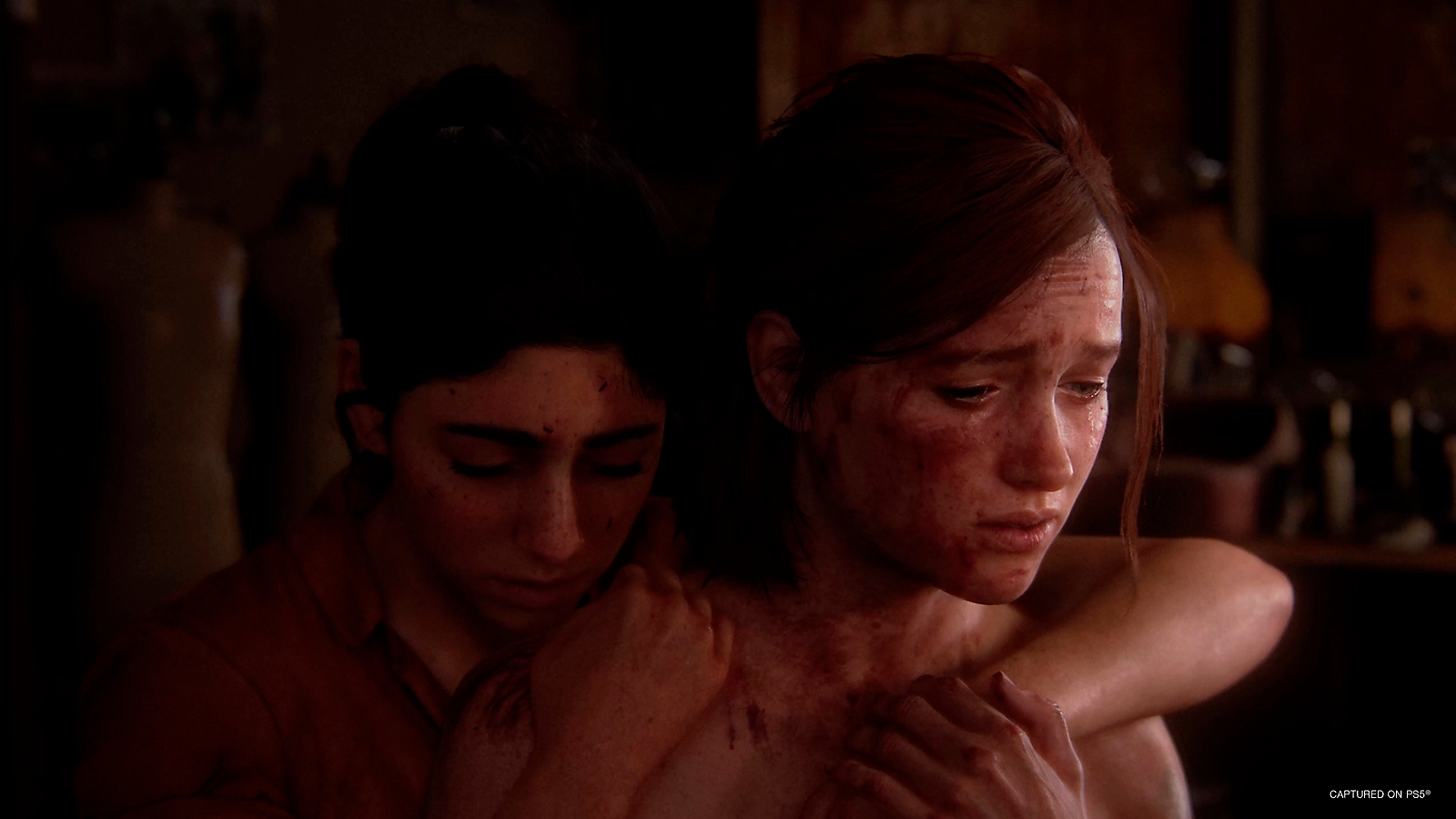 Dos personas abrazándose, con sangre en sus rostros. Ambiente oscuro e íntimo.