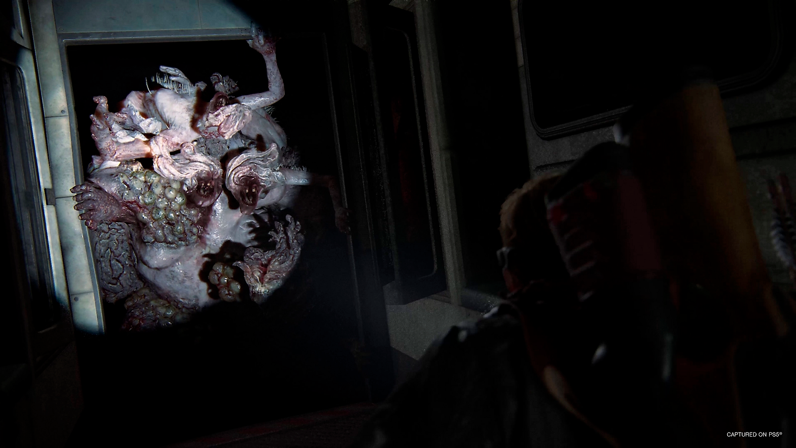 Escena oscura de un juego. Un monstruo en una puerta y una persona apunta con un arma.