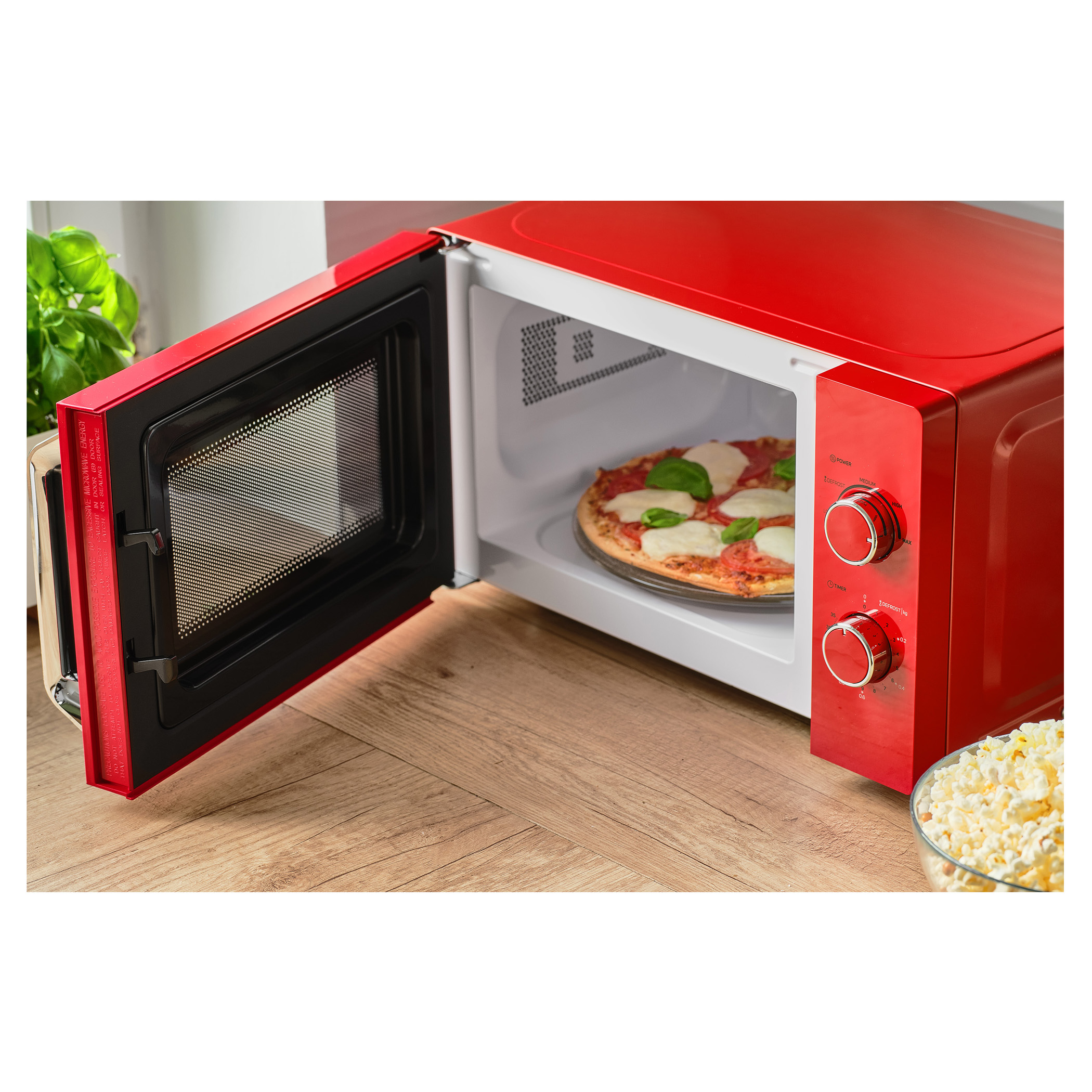 Piros mikrohullámú sütő pizzával belül és nyitott ajtóval. Sajt egy tálban a fa felületen.