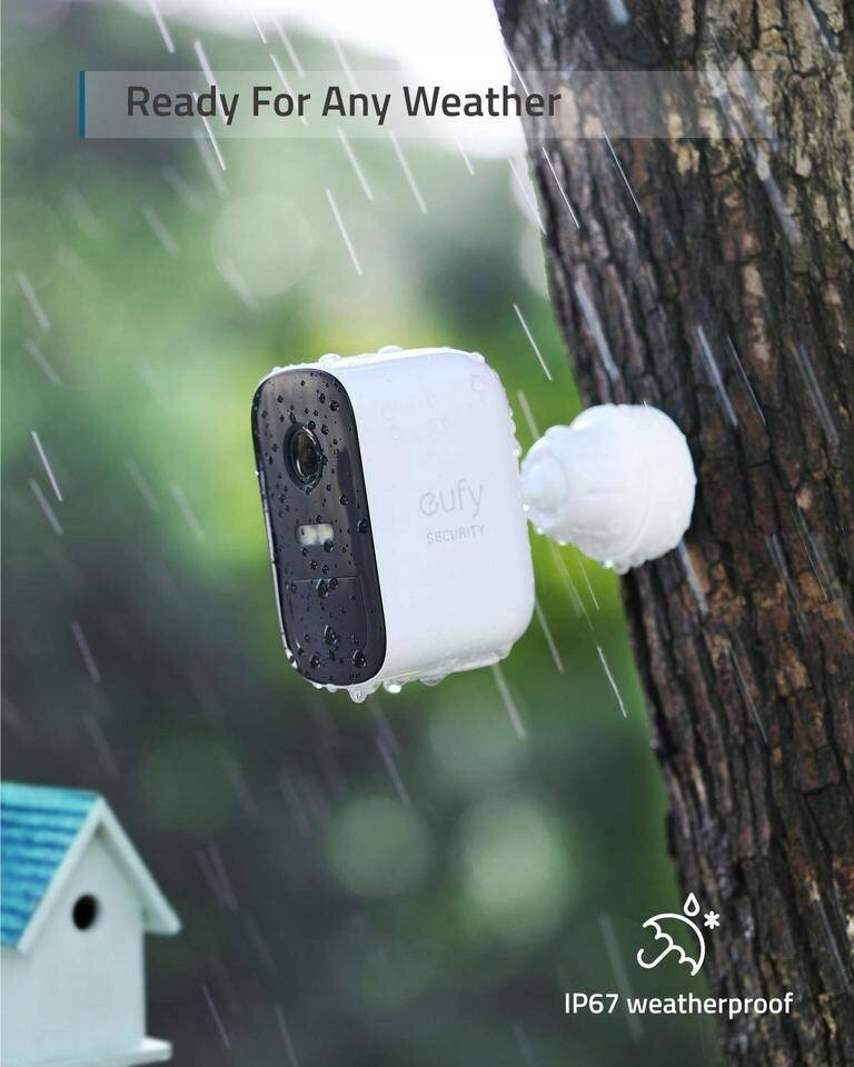 Biała kamera bezpieczeństwa zamontowana na drzewie, pada deszcz. Tekst mówi 'Ready For Any Weather' i 'IP67 waterproof'.
