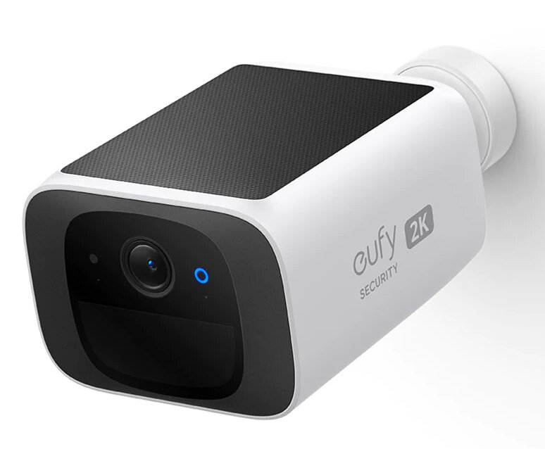 Biała kamera bezpieczeństwa zamontowana na ścianie. Panel słoneczny na górze, czarna obwódka, niebieskie światło.