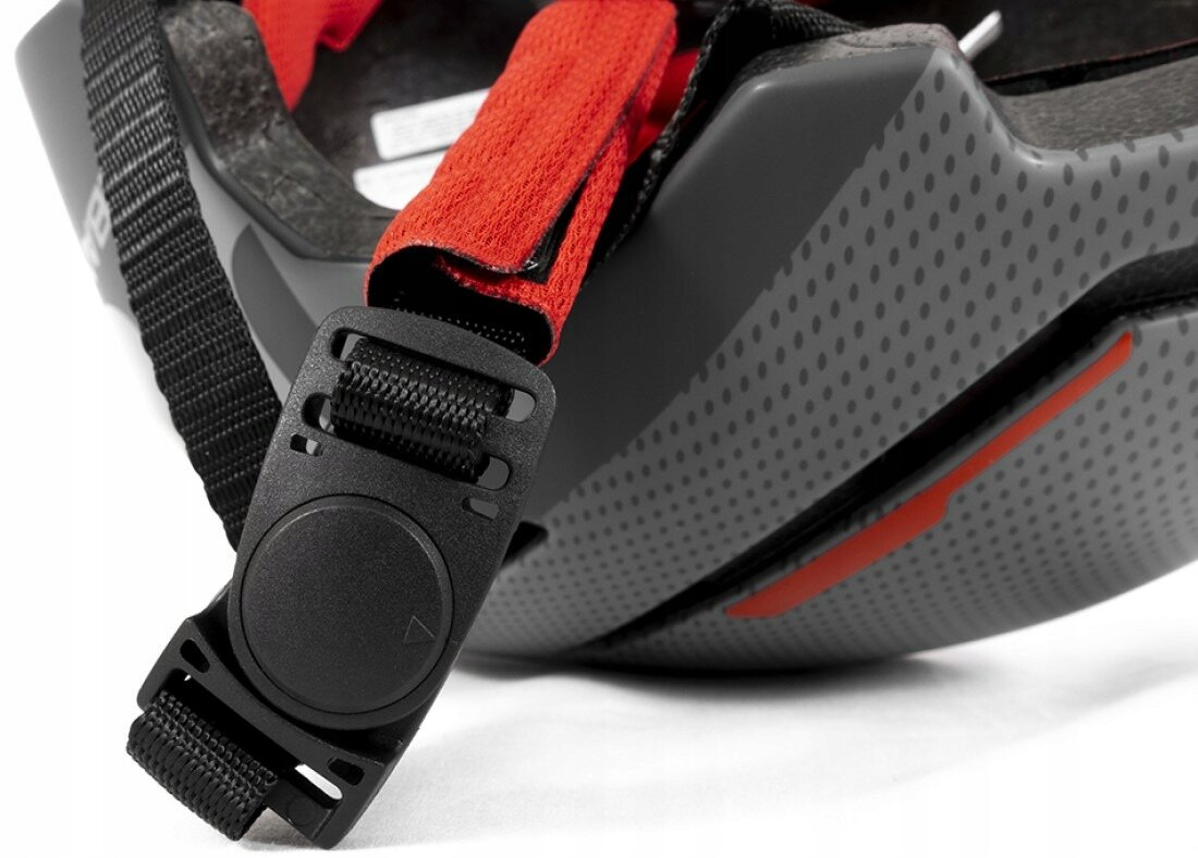 Zbliżenie czarnego kasku z czerwonym paskiem i sprzączką regulacyjną.