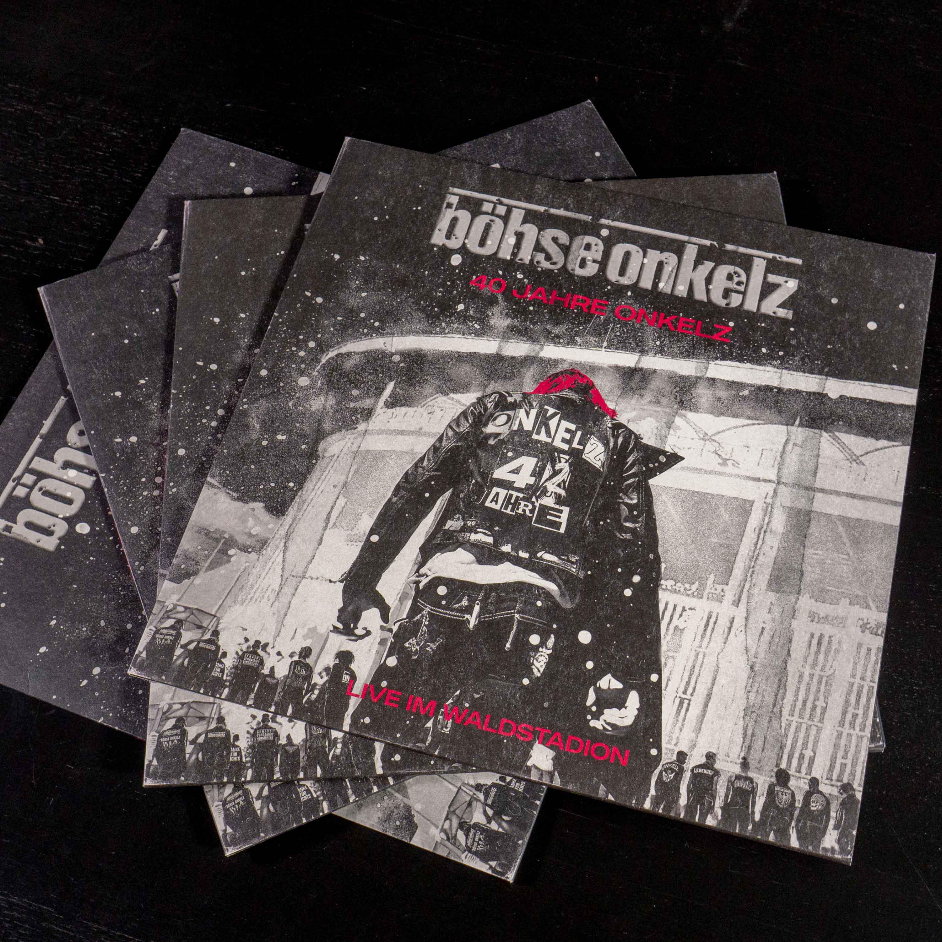 Stapel von CDs mit schwarz-weißem Albumcover. Die oberste CD zeigt eine Figur und Text.
