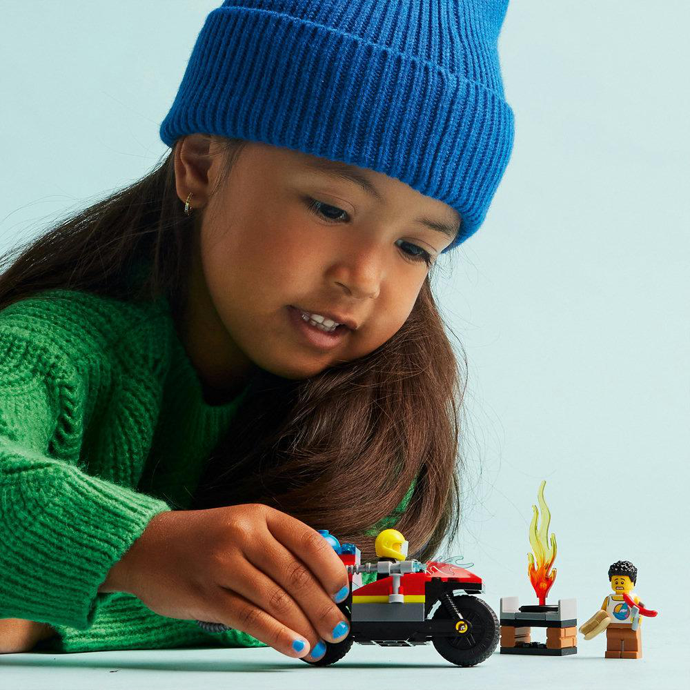 Junges Mädchen spielt mit einem LEGO-Spielzeug. Sie hält ein rotes Motorrad und eine Minifigur.