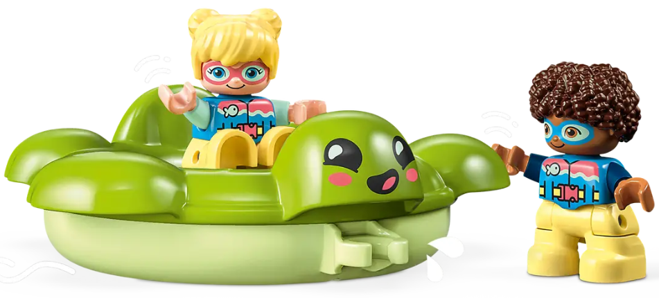 Dwie figurki Lego na zielonej łodzi w kształcie żółwia, jedna macha. Obok stoi kolejna figurka.