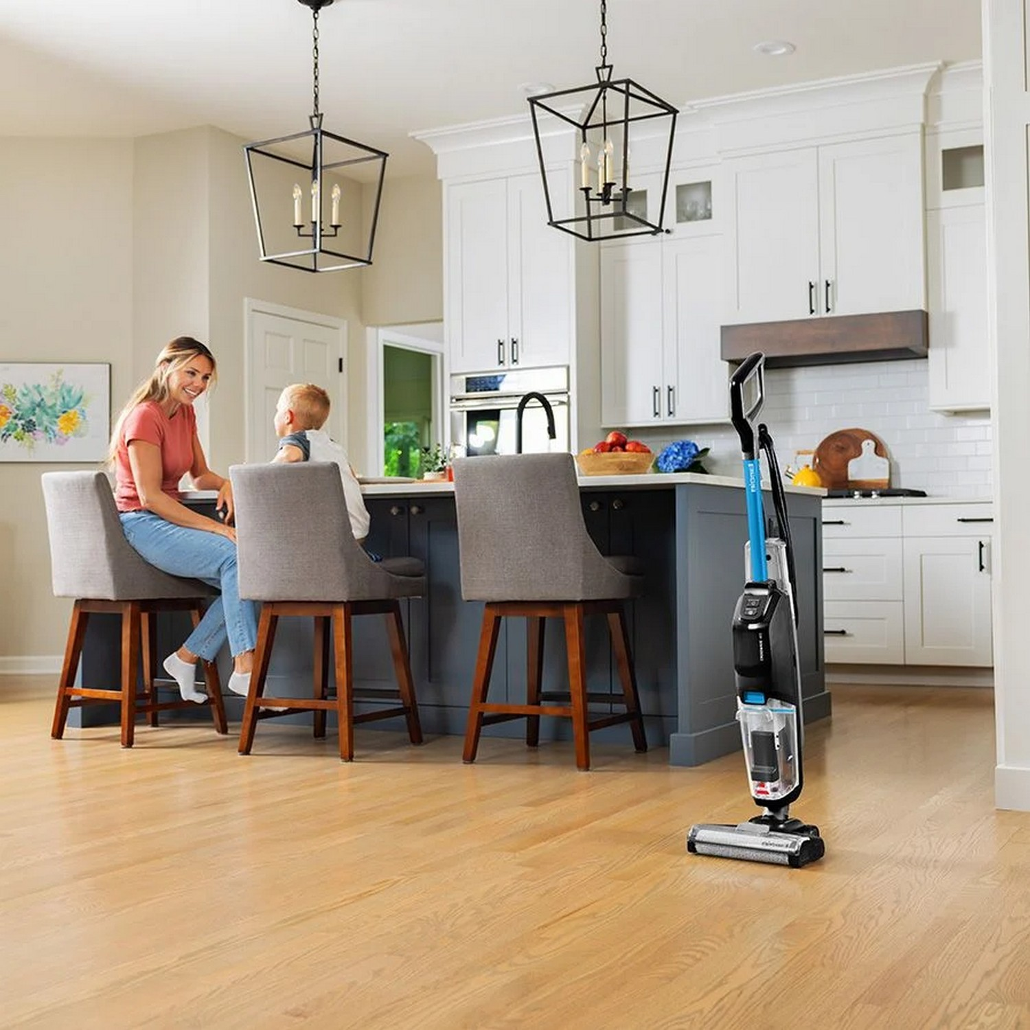 Femme et enfant à l'îlot de cuisine, machine de nettoyage au premier plan.