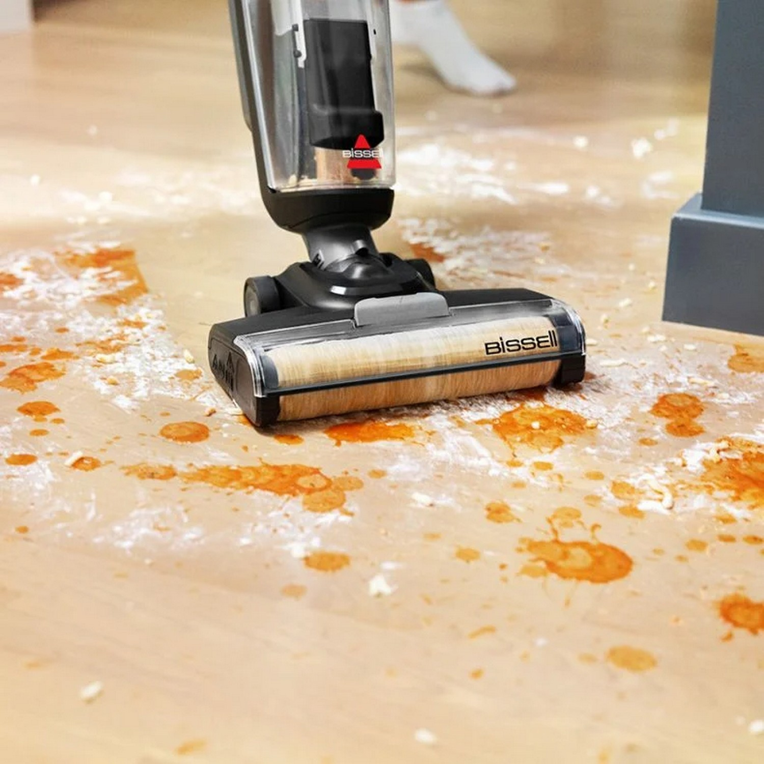 Un aspirateur Bissell nettoyant un plancher en bois, avec des taches oranges.