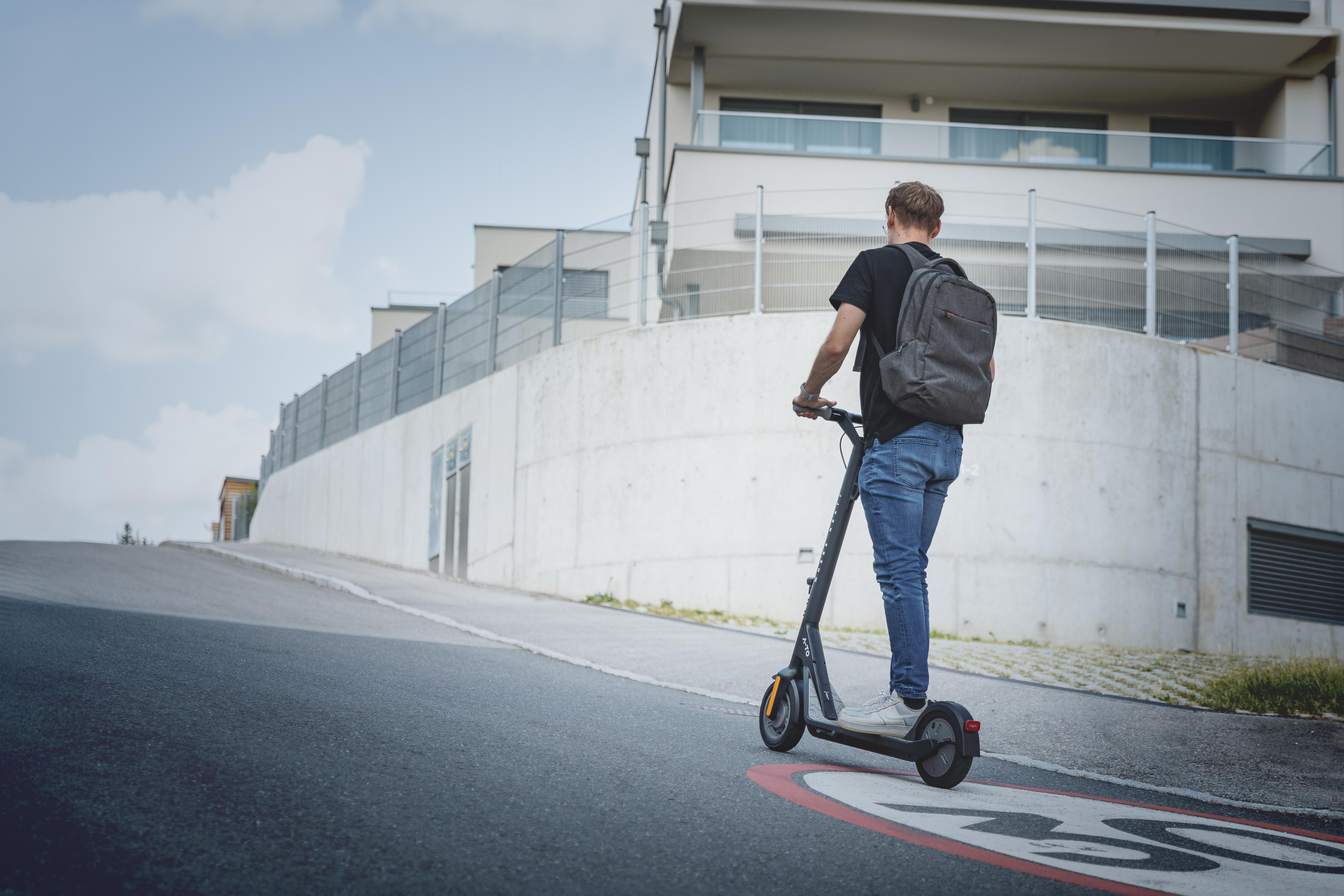 Mann fährt mit einem E-Scooter auf einer Straße.