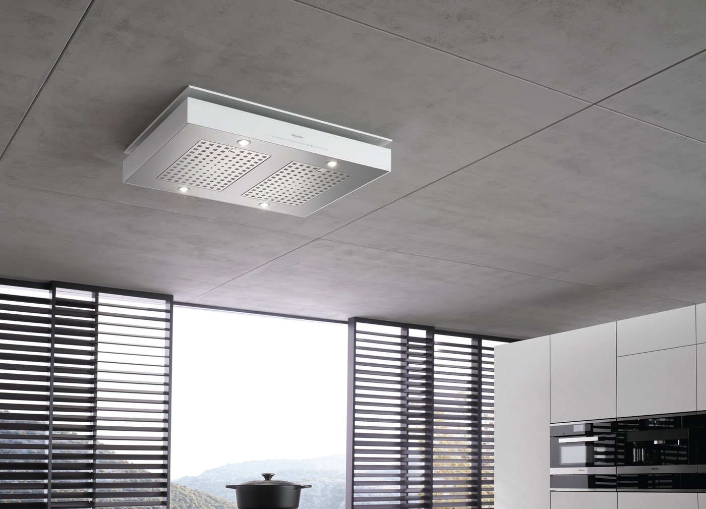 Eine Dunstabzugshaube aus Metall und Weiß hängt an einer Betondecke über einem Herd.
