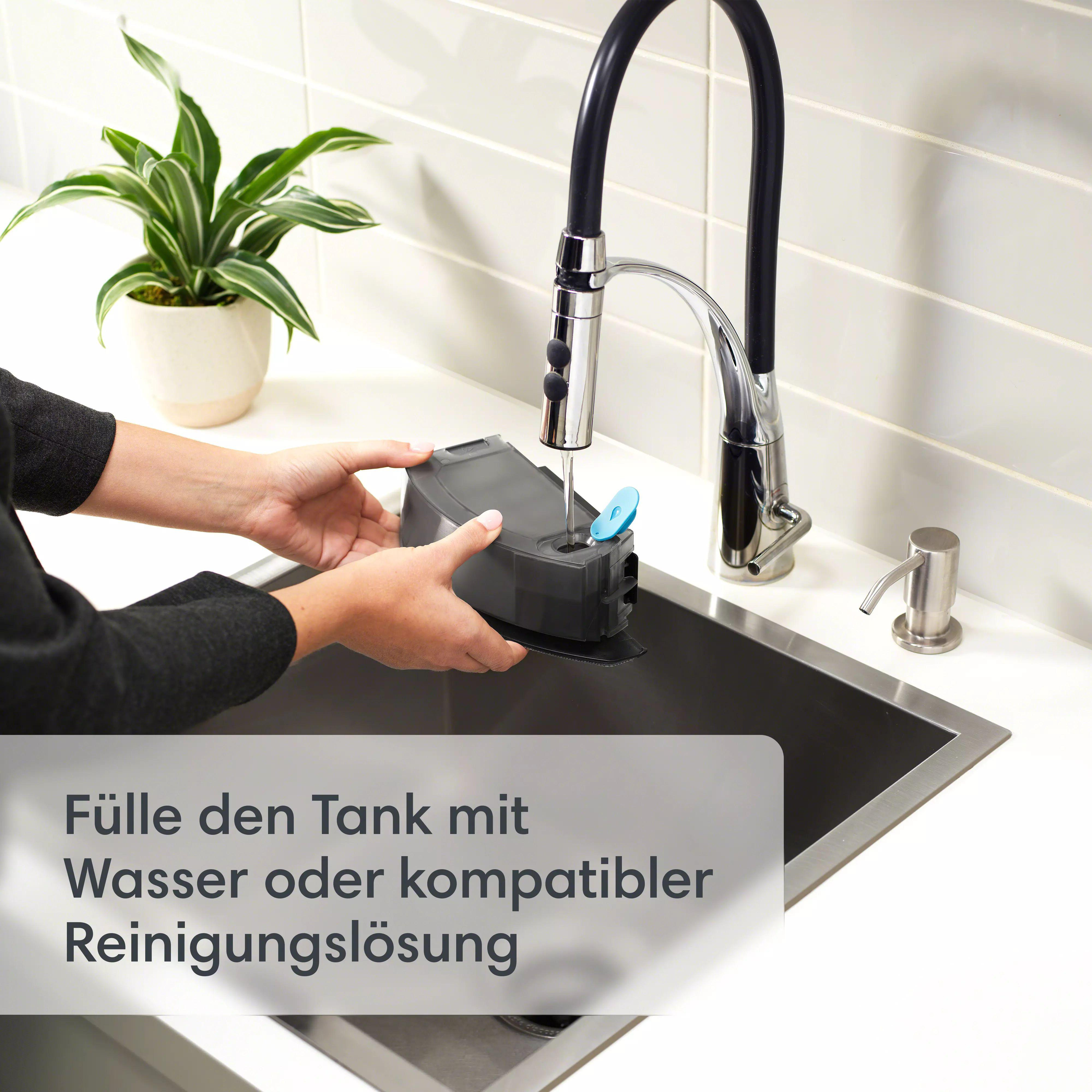 Hände, die einen schwarzen Behälter unter einem Wasserhahn befüllen. Pflanze im Topf und Seifenspender sichtbar.