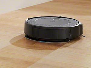 Ein schwarzer und grauer Roboter-Staubsauger auf einem Holzboden. Der Staubsauger ist rund und hat ein niedriges Profil.