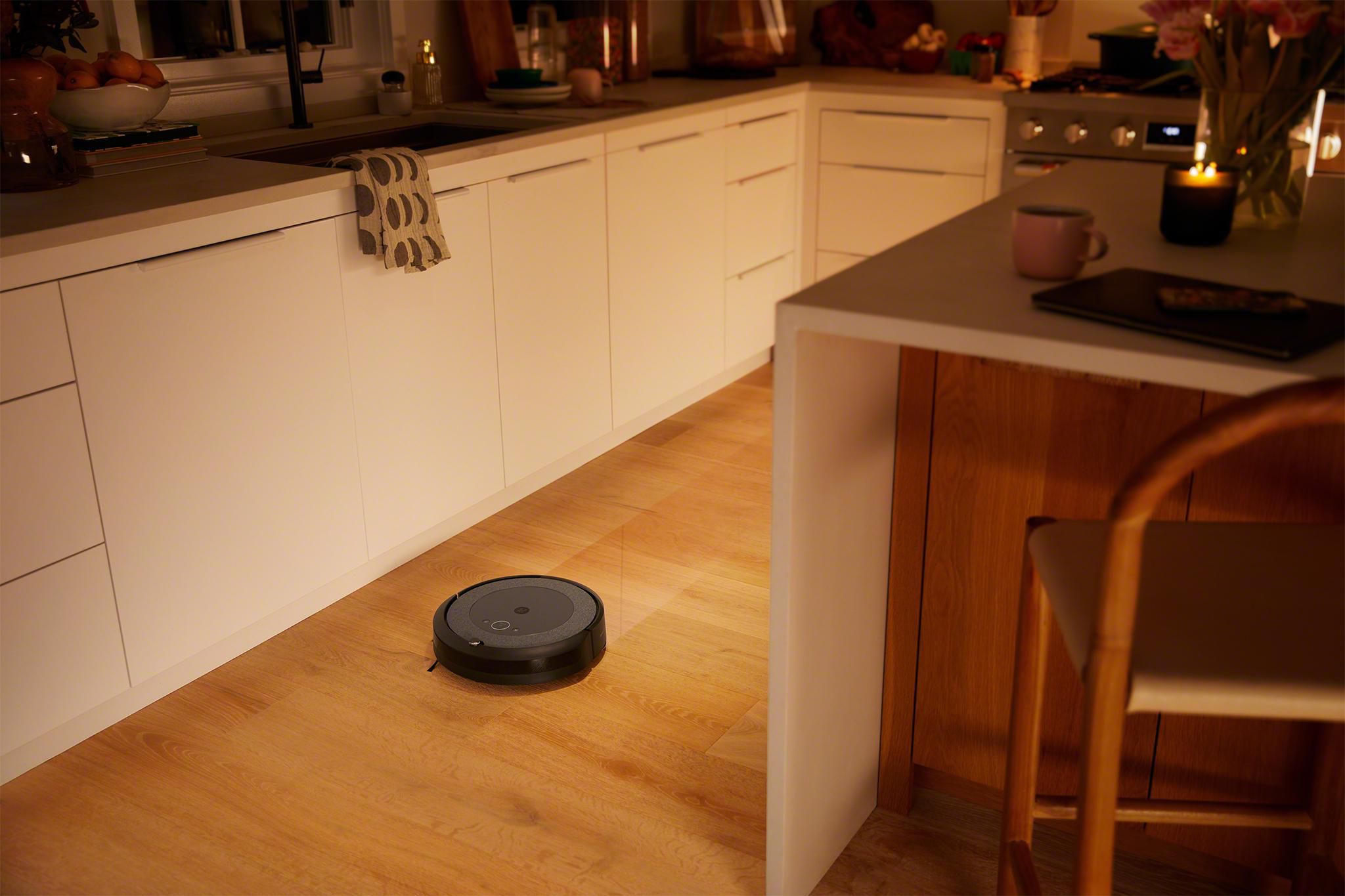 Ein Roboter-Staubsauger reinigt eine Küche mit Holzböden. Weiße Schränke und eine Arbeitsplatte sind sichtbar.
