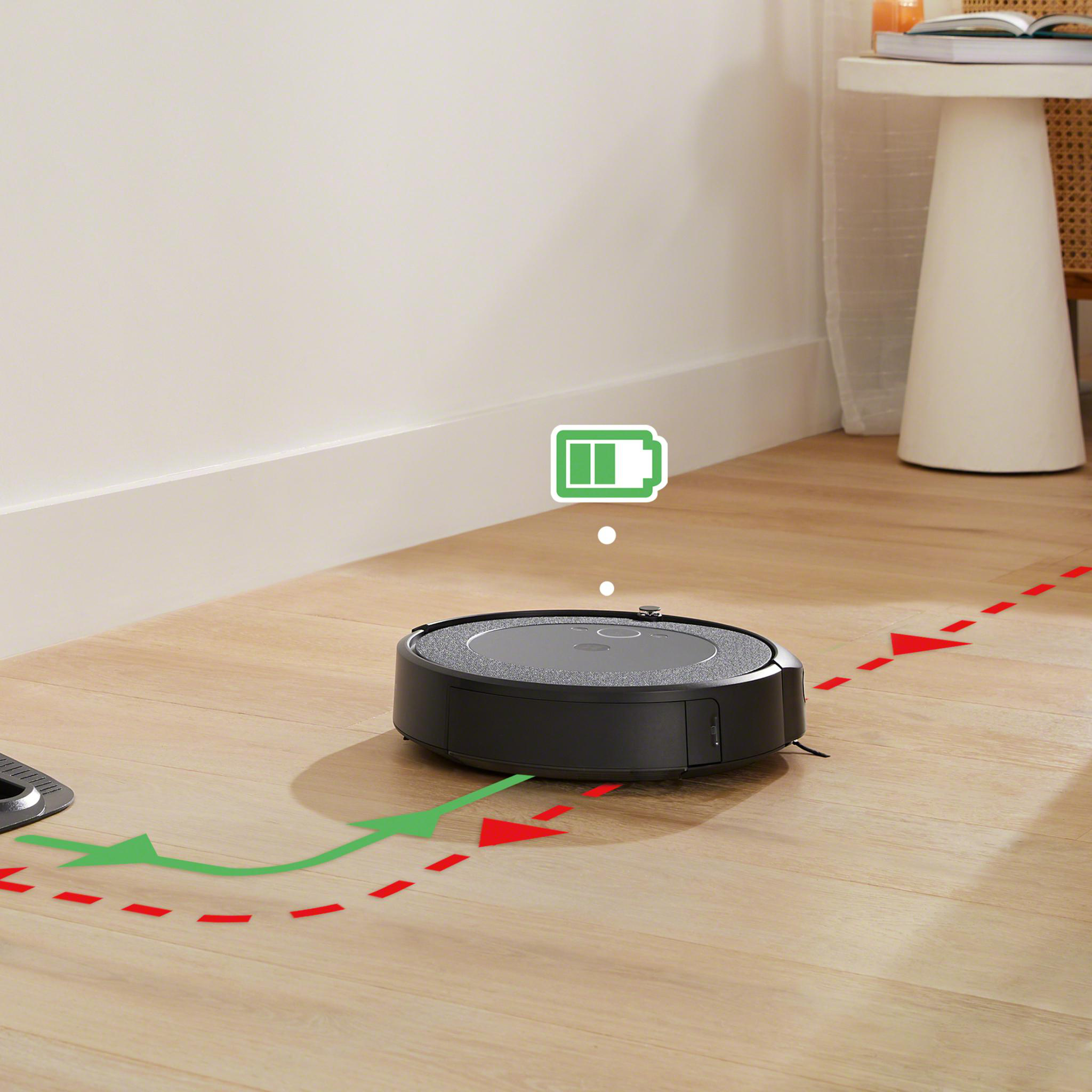 Ein schwarzer Roboter-Staubsauger auf einem Holzboden. Ein grünes Batteriesymbol zeigt den Ladestatus an.