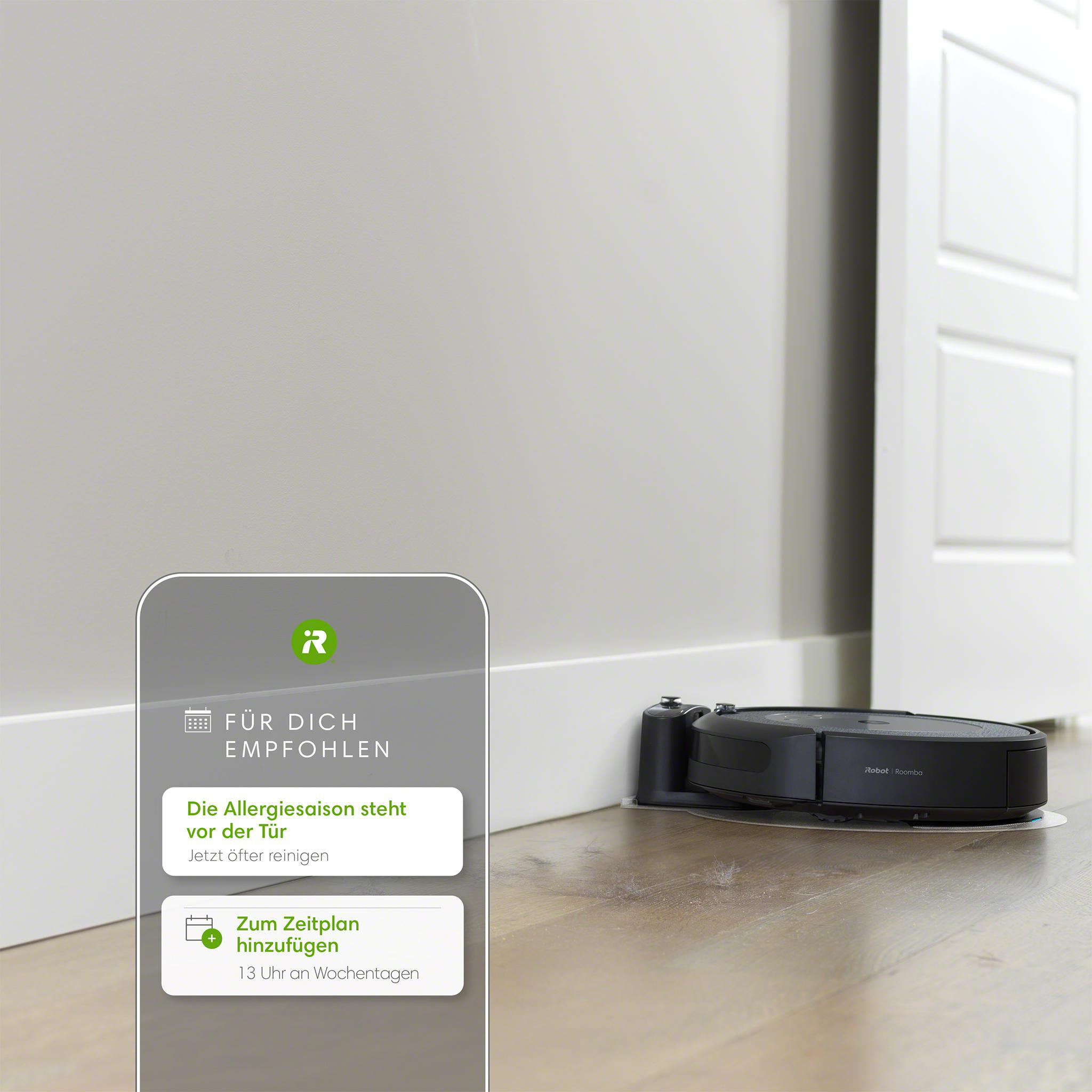 Roboter-Staubsauger auf Holzboden, nahe Wand und Tür. App-Oberfläche sichtbar.