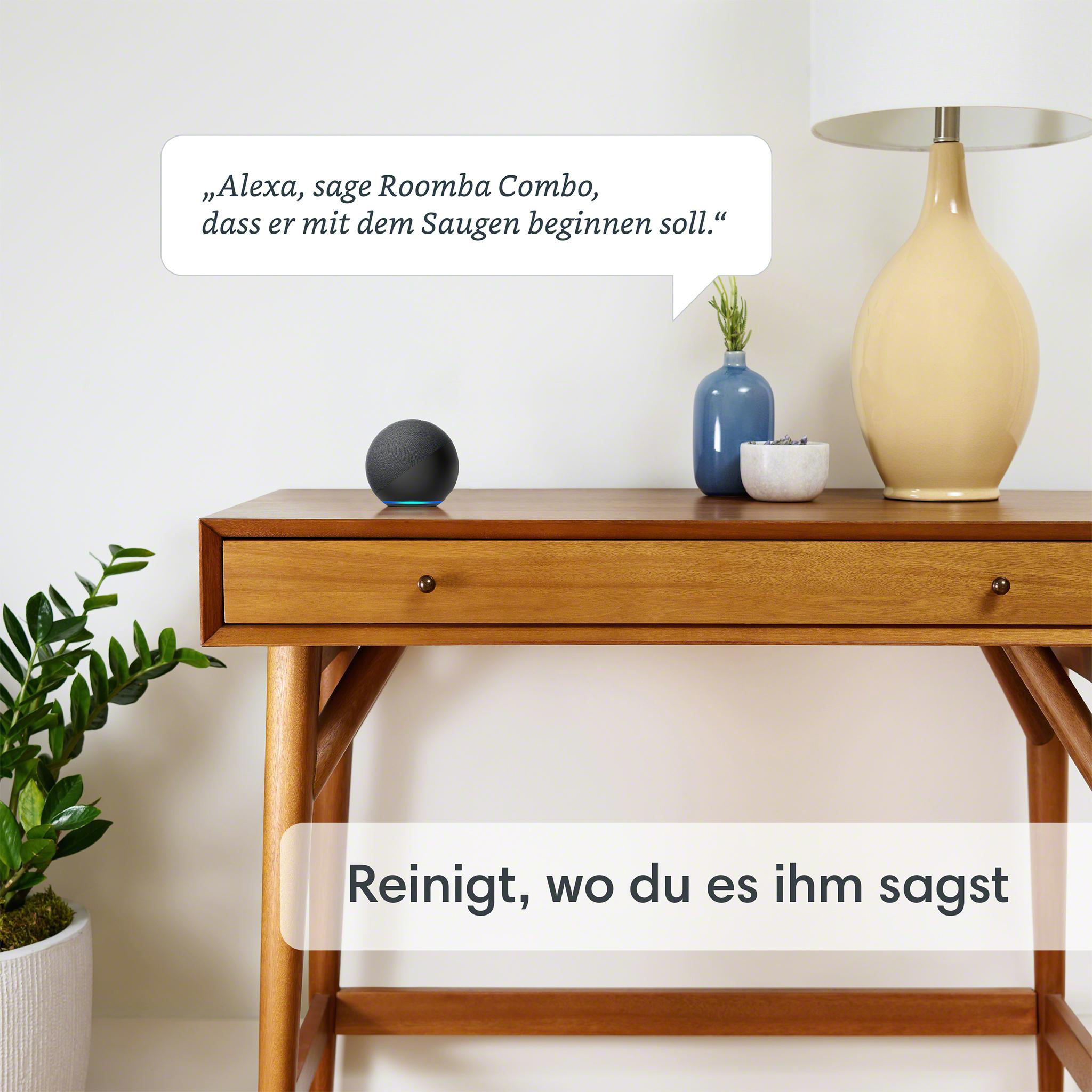 Ein schwarzer Smart Speaker auf einem Holztisch, mit Pflanze, Vase und Lampe, mit deutschem Text.