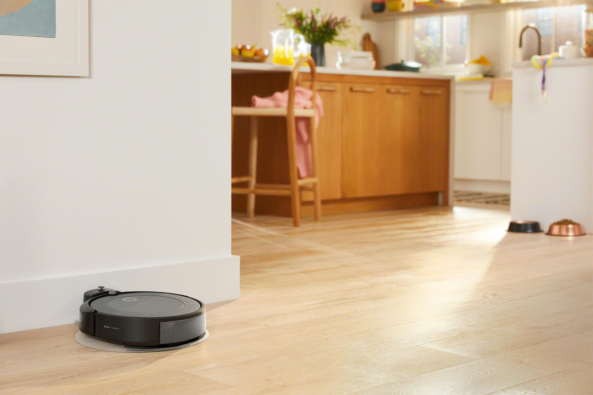 Ein schwarzer Roboter-Staubsauger auf Holzboden, nahe Wand und Küche.