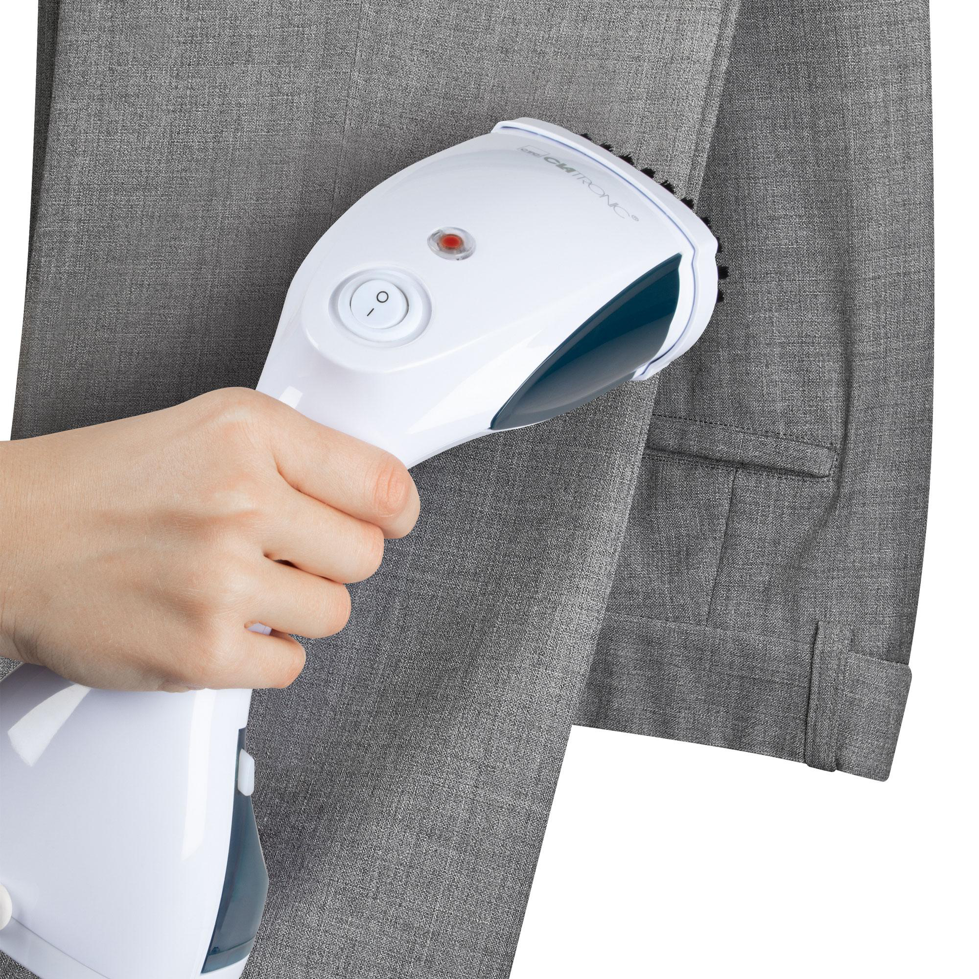 Ein weißer Kleidungsdampfer wird an einer grauen Hose verwendet, die von einer Hand gehalten wird.