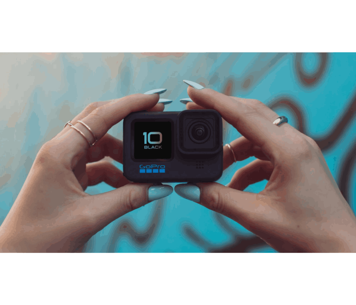 Manos sosteniendo una cámara GoPro negra, mostrando la pantalla. Fondo azul con diseño de graffiti.