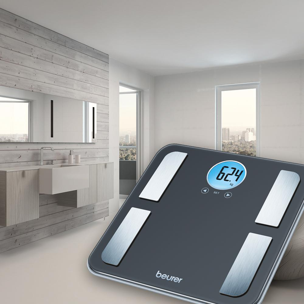 Eine Digitalwaage mit 62,4 kg. Die Waage ist schwarz mit silbernen Akzenten, in einem Badezimmer.
