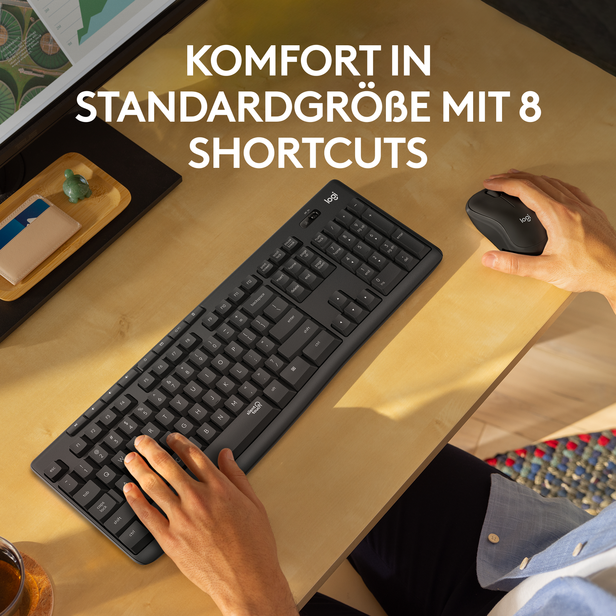 Eine schwarze Tastatur, Maus und Monitor auf einem Holztisch. Text sagt 'Komfort in Standardgröße'.