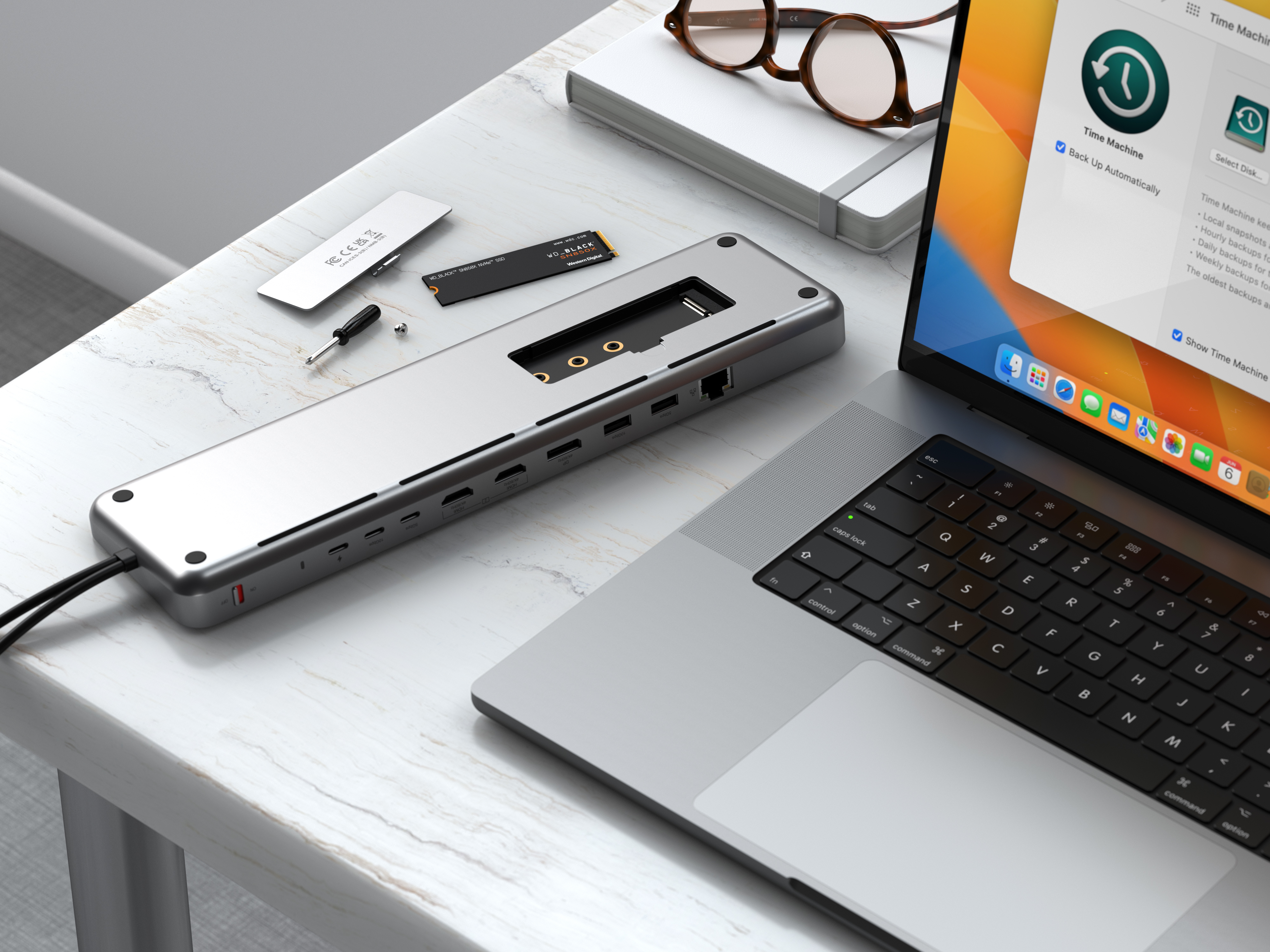 Laptop, Dockingstation und Zubehör auf dem Schreibtisch. Graue Station, weißer Laptop. Modernes Büro.