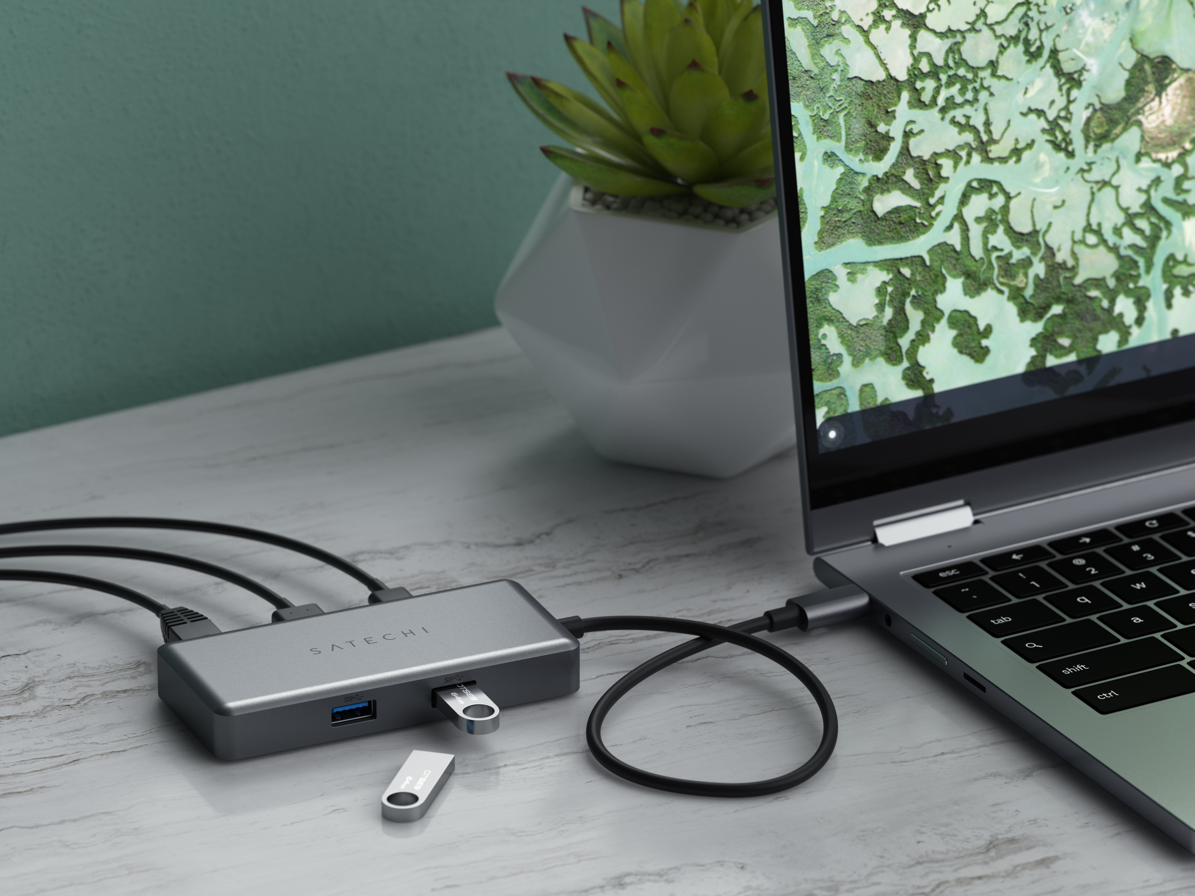Laptop mit Hub und USB-Laufwerken auf Marmor, Pflanze im Hintergrund.