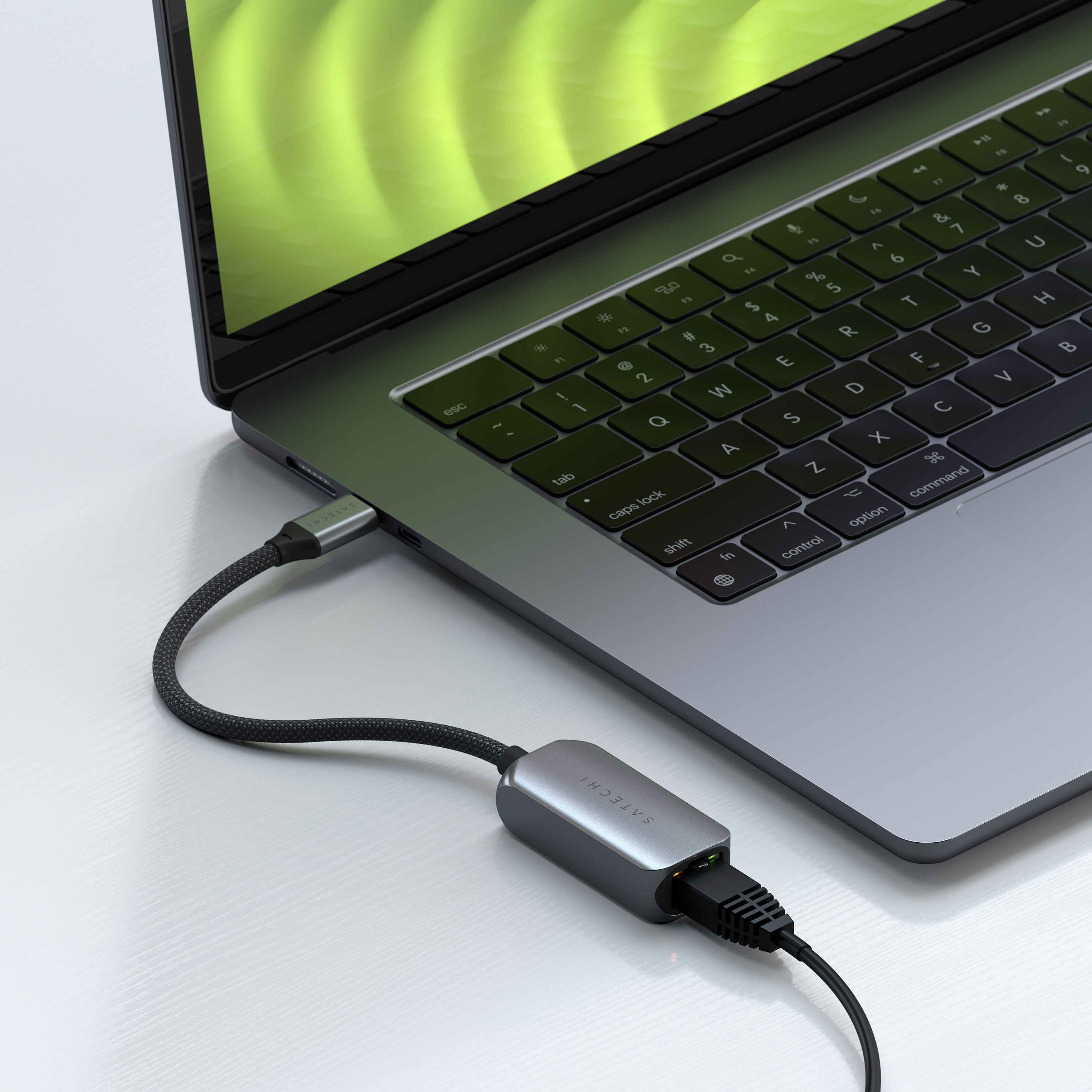 Laptop collegato a un adattatore Ethernet. Adattatore e cavo neri e grigi. Laptop con schermo verde. Superficie bianca.