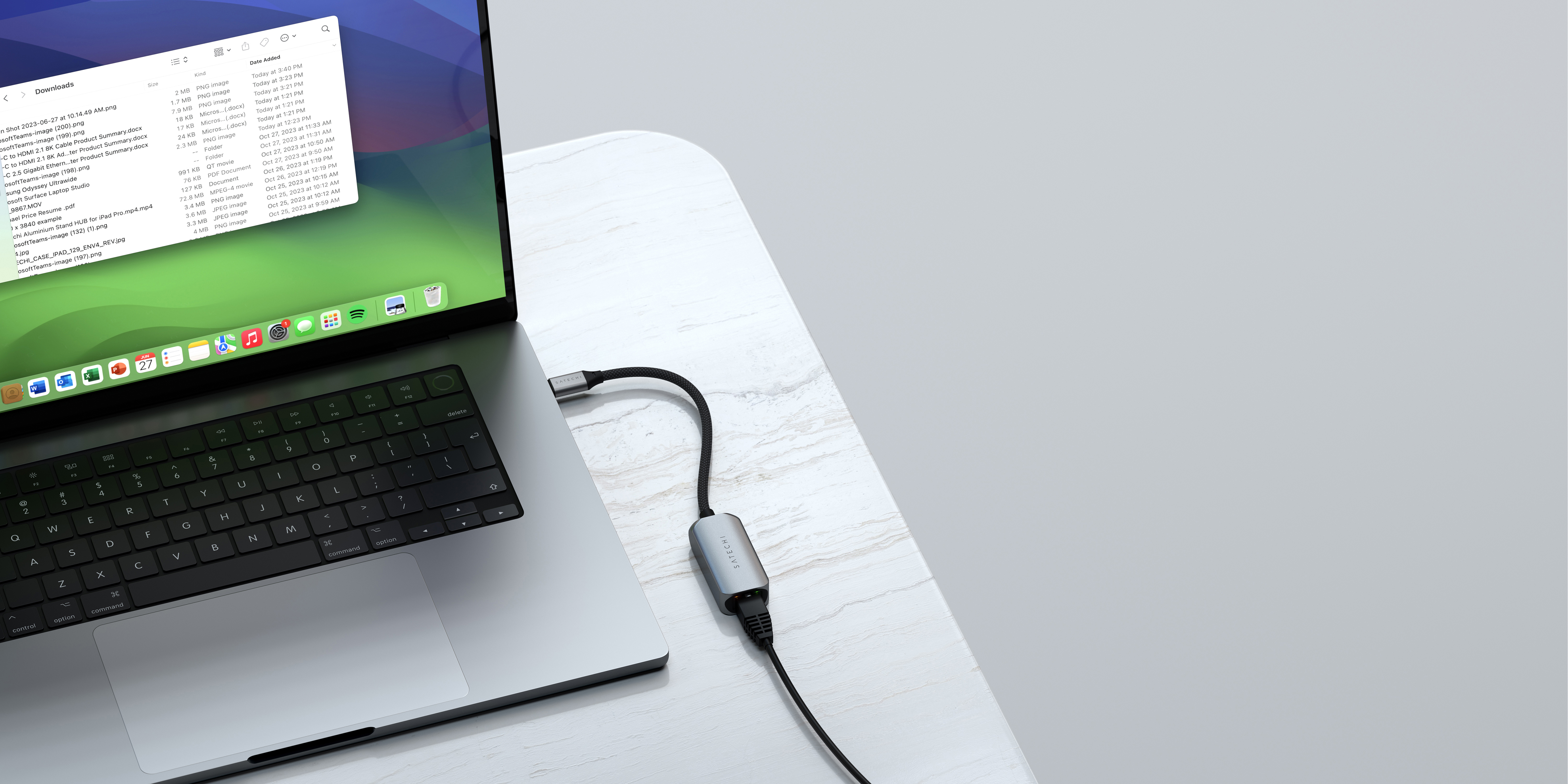 Laptop collegato a un adattatore argentato e un cavo USB su una superficie bianca.