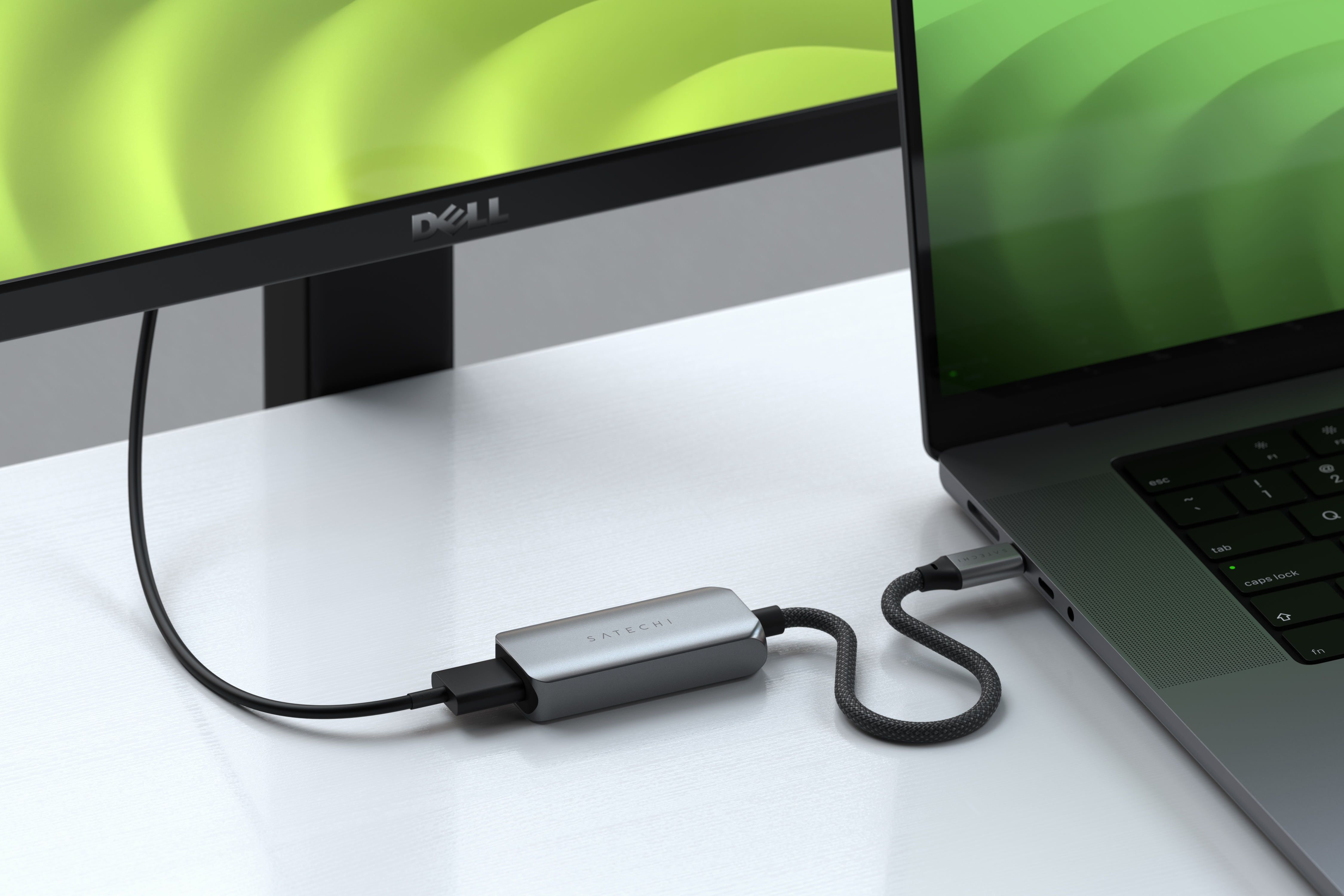 Silberner Satechi-Adapter mit Laptop und Monitor verbunden. Kabel auf weißem Schreibtisch sichtbar.