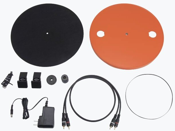 Elementy gramofonu. Zawiera czarne i pomarańczowe talerze, przewody, zasilacz i rysik.