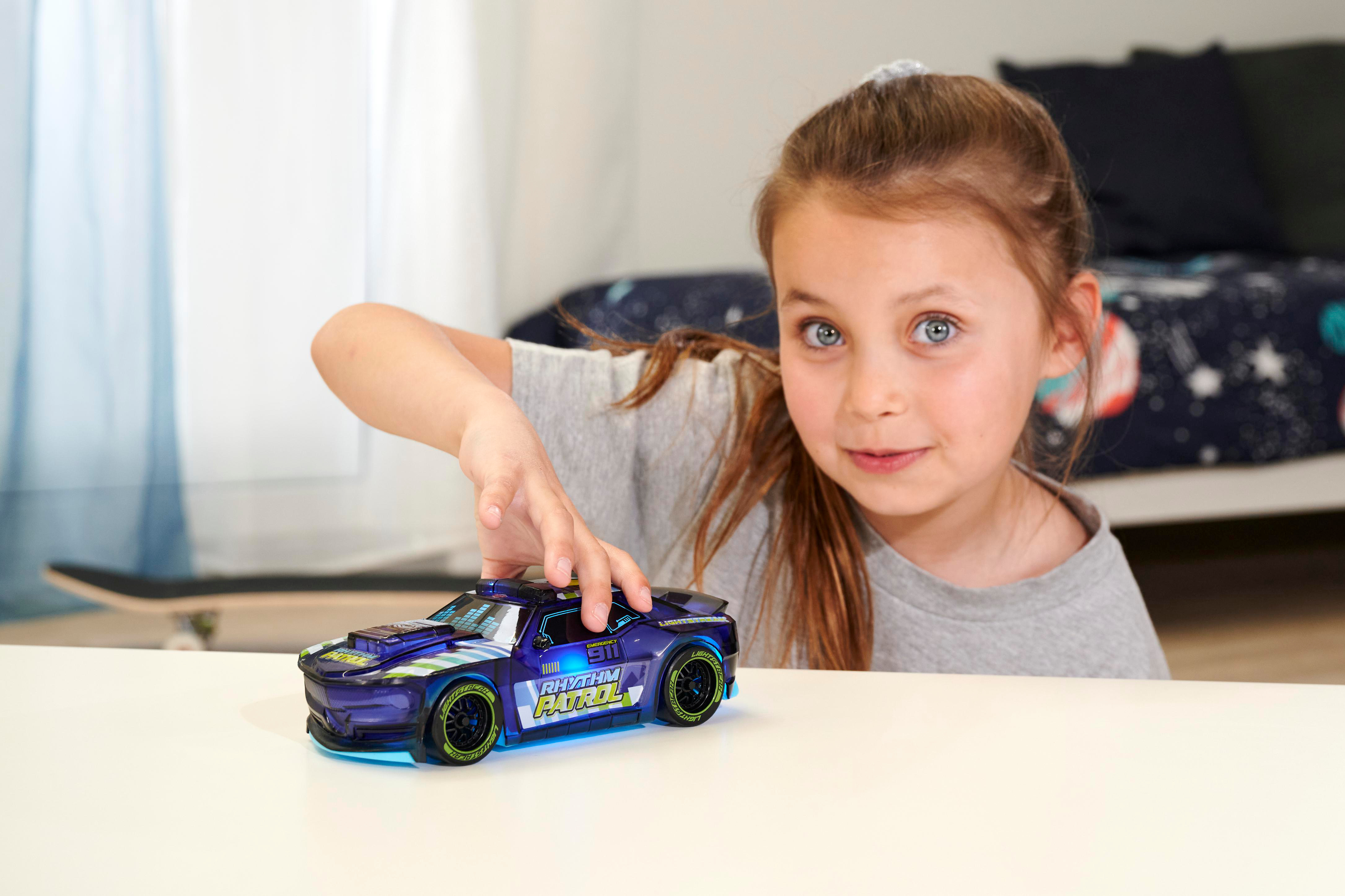 Ein junges Mädchen greift nach einem Spielzeugauto auf einem weißen Tisch in einem Raum.