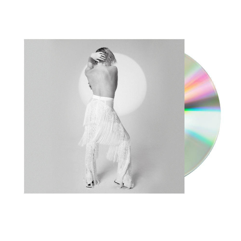 Egy fehér bojtos nadrágos és felsős nő egy CD közelében áll. Ő egy reflektorfényben van.