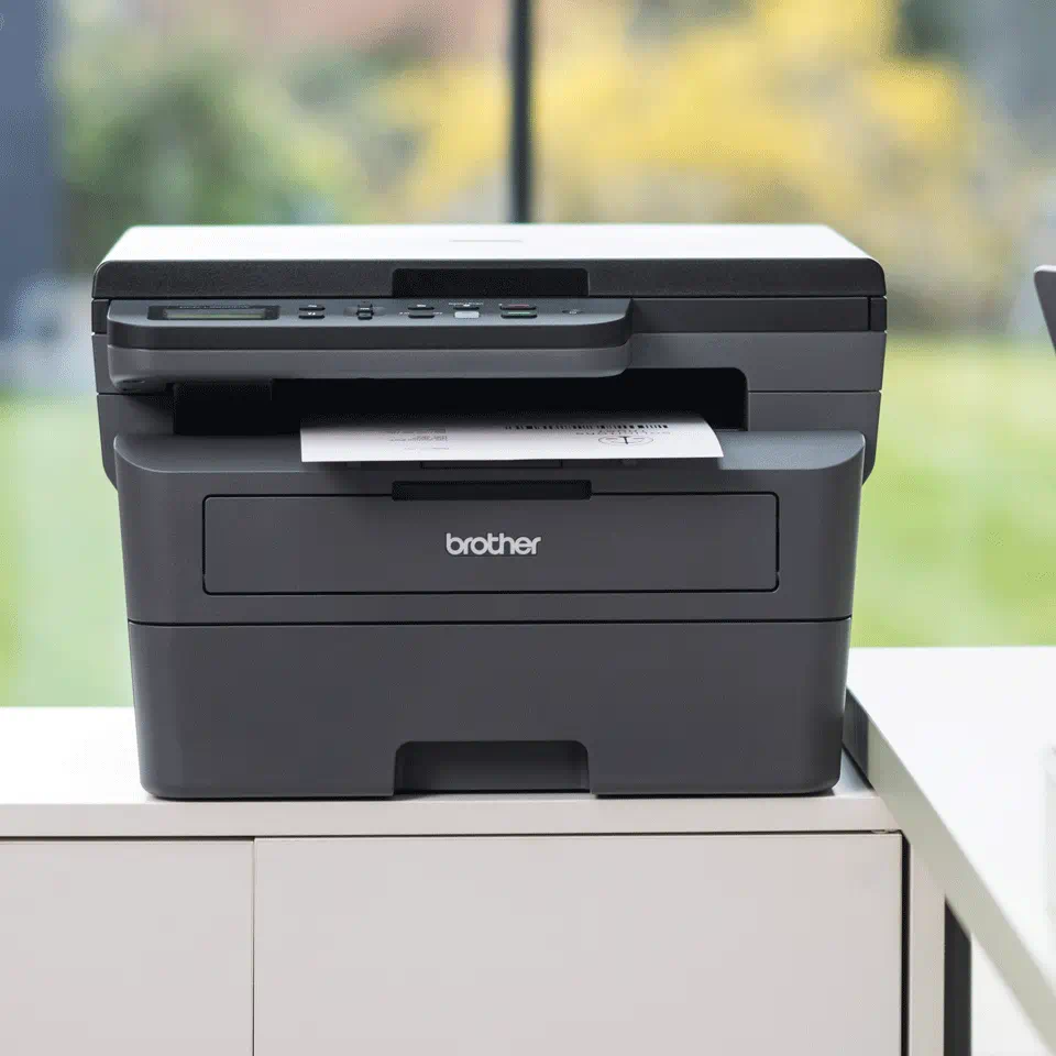 Ein schwarz-grauer Drucker auf einer weißen Oberfläche. Ein Papier kommt heraus.