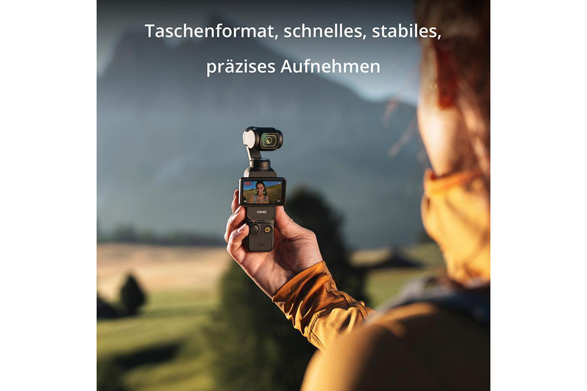 Eine Person hält eine Kamera, mit einer Berglandschaft im Hintergrund.