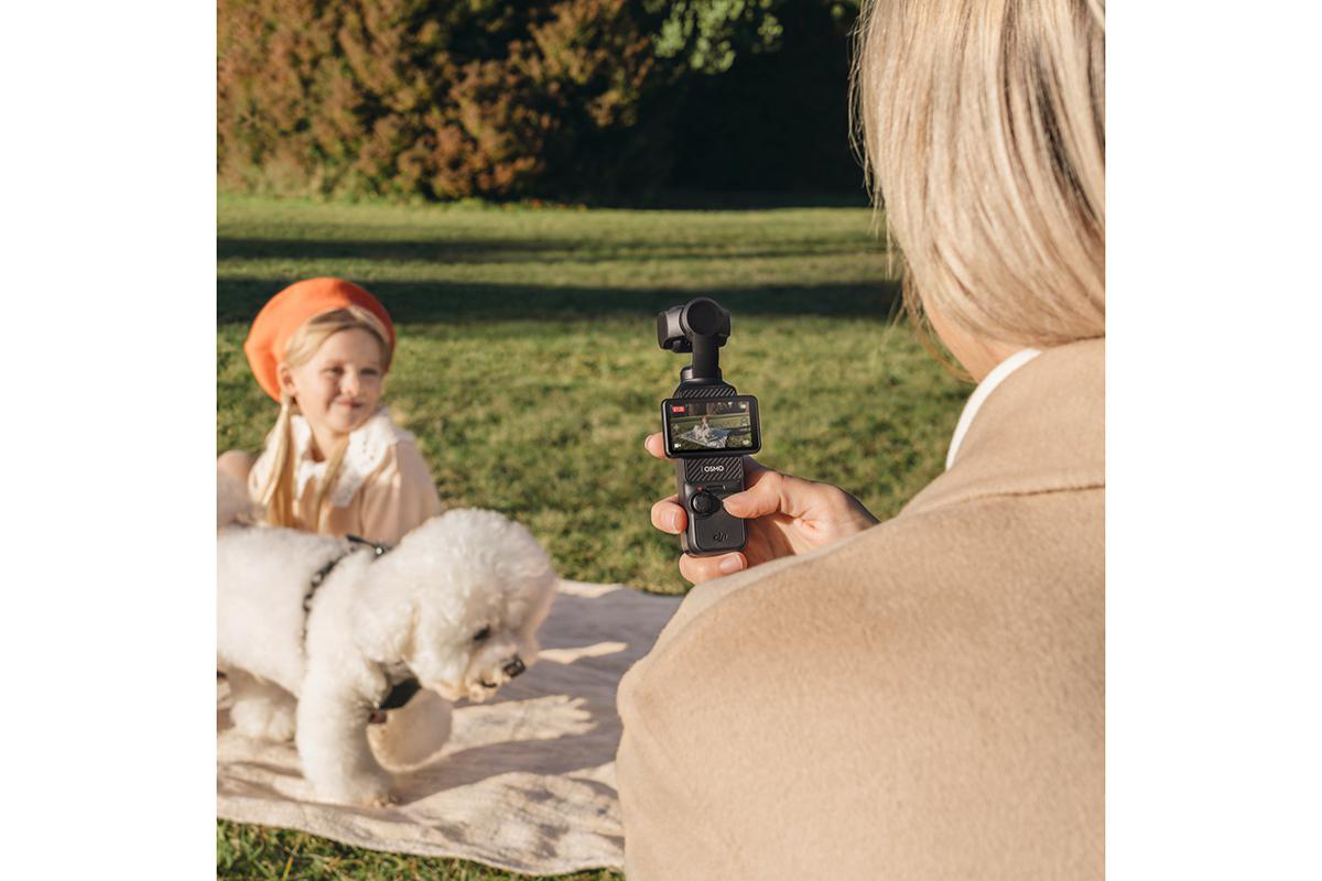 Eine Frau hält eine Taschenkammera und filmt ein Mädchen und einen Hund in einem Park.